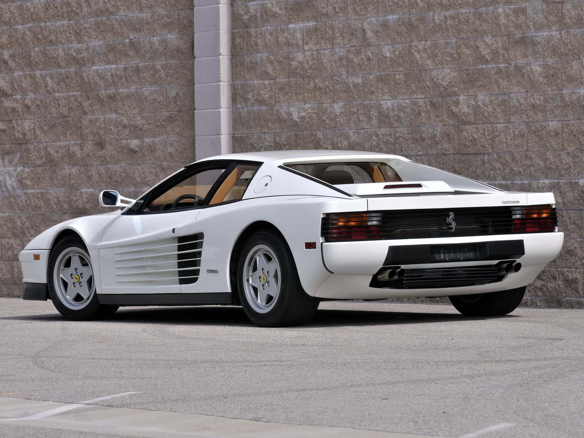 Ferrari Testarossa 桌布 壁紙 — 一輛純白色的法拉利 Testarossa 以傾斜角度停放在質感石牆旁，地面為鋪砌路面。