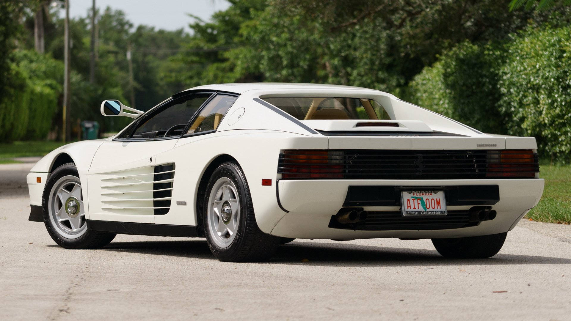 white ferrari 桌布 壁紙 — 一輛純白色的法拉利 Testarossa 停泊在鋪砌的道路上，周圍環繞著茂密的綠樹。