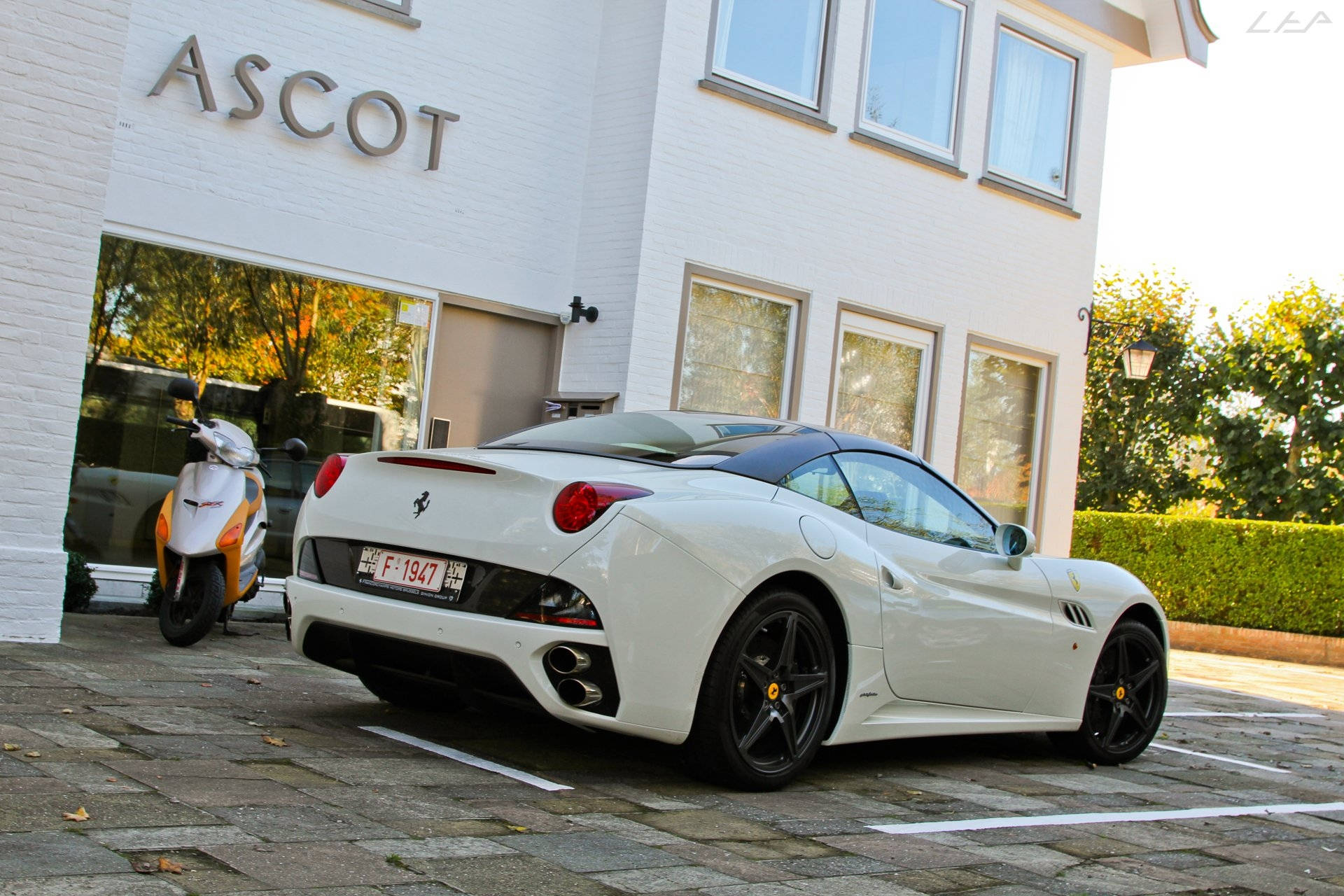 white ferrari 桌布 壁紙 — 一輛純白色的法拉利加利福尼亞停在高級建築前，秋天的樹木倒映在玻璃窗上。
