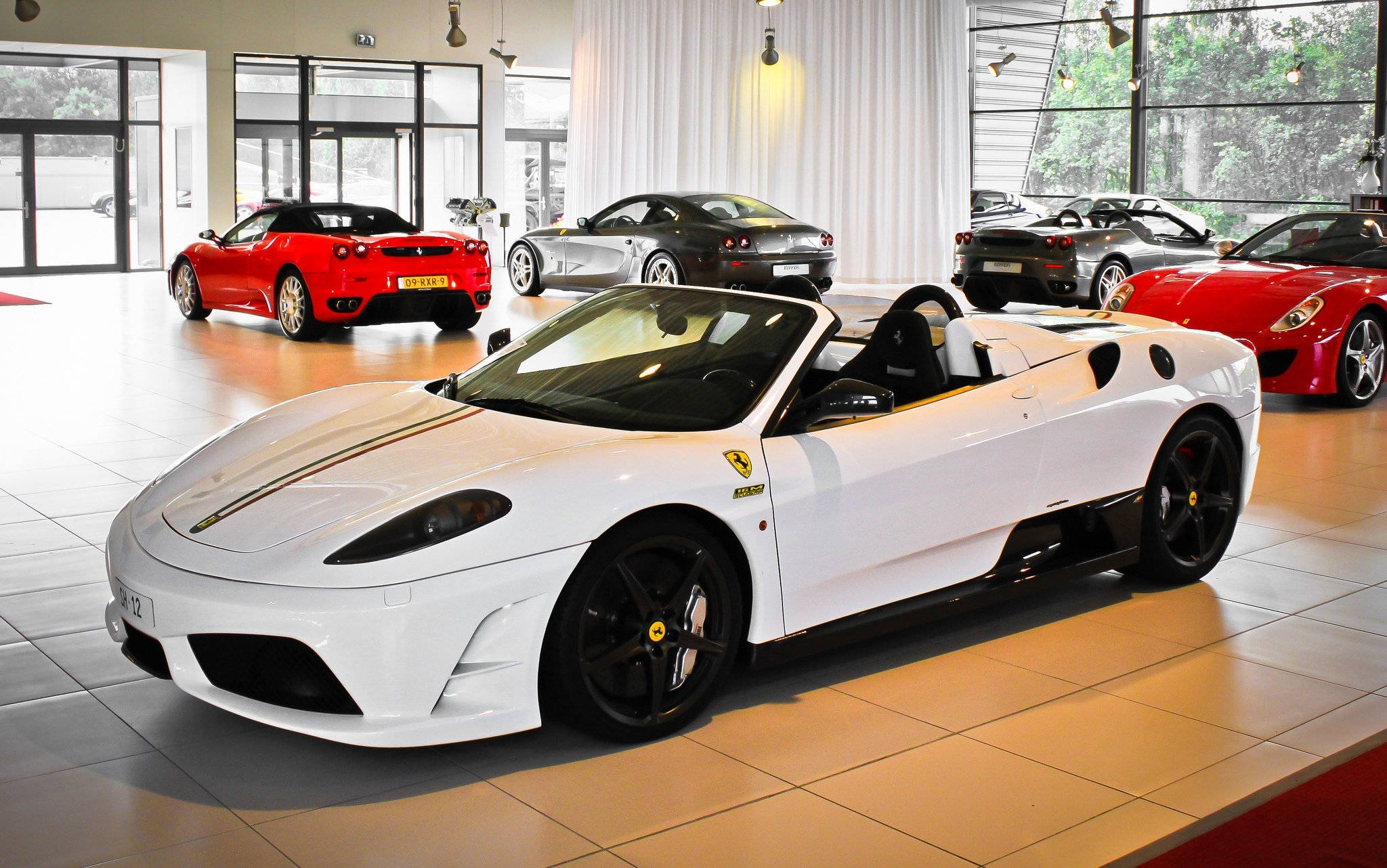 white ferrari 桌布 壁紙 — 一輛純白色的法拉利敞篷車在明亮的燈光下閃耀，與其他鮮紅色和銀色的法拉利一同展示在豪華車展廳中。