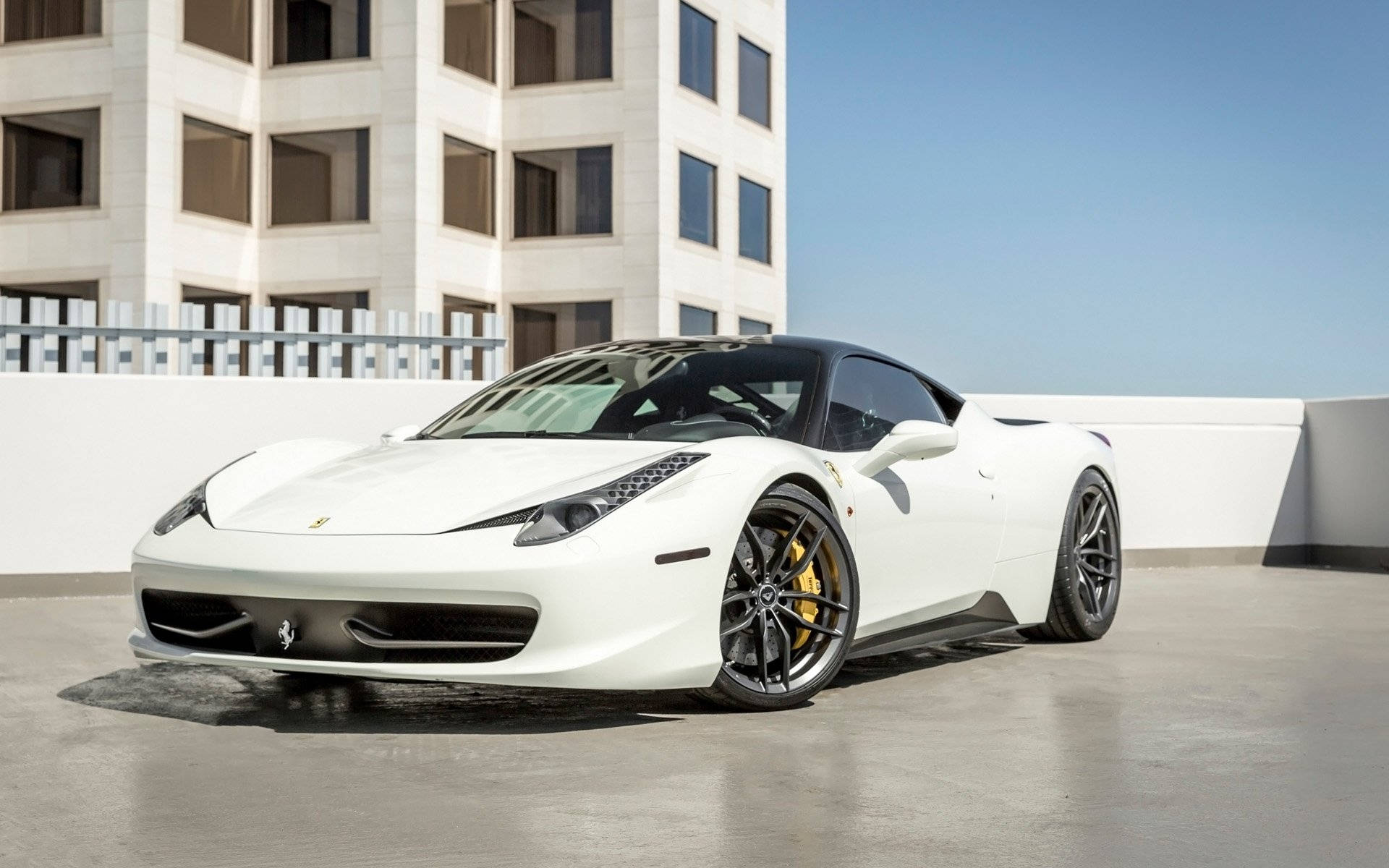 white ferrari 桌布 壁紙 — 一輛純白色的法拉利跑車，帶有黑色飾件和金色制動卡鉗，停泊在現代建築物的屋頂上，背景是晴朗的藍天。