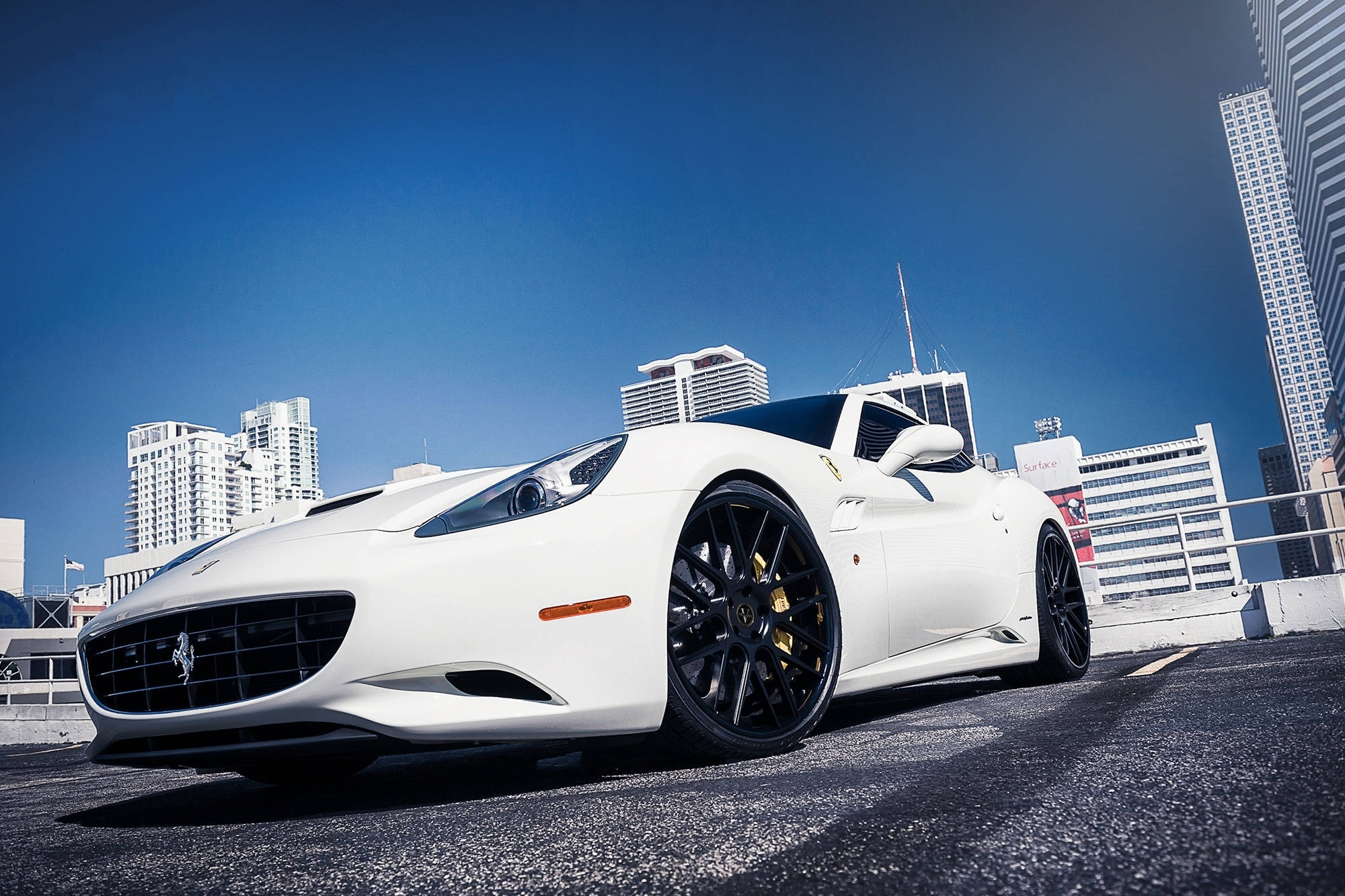 white ferrari 桌布 壁紙 — 一輛純白色的法拉利跑車停泊在陽光明媚的城市橋樑上，摩天大樓在清澈的藍天下高聳入雲。