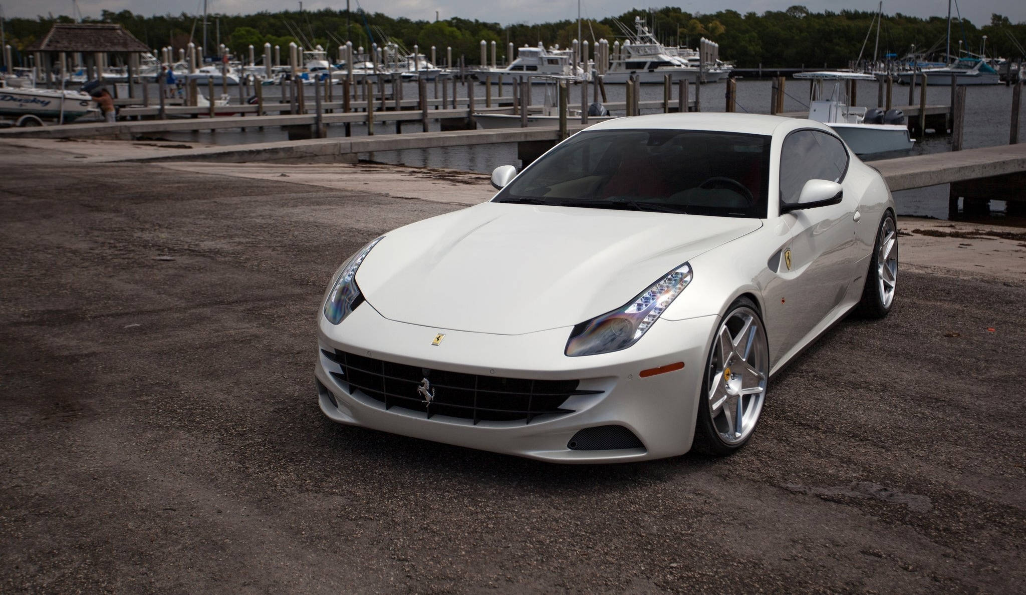 white ferrari 桌布 壁紙 — 一輛純白色的法拉利跑車在碼頭上閃閃發光，背景有船隻和樹木。