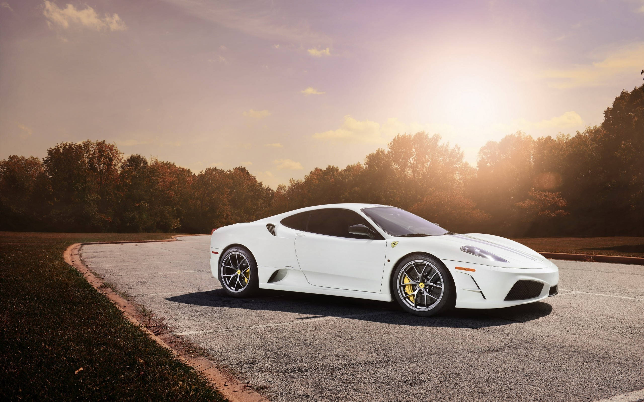 white ferrari 桌布 壁紙 — 一輛純白色的法拉利跑車在蜿蜒的道路上閃閃發光，背景是金色的日落和秋天的樹木。