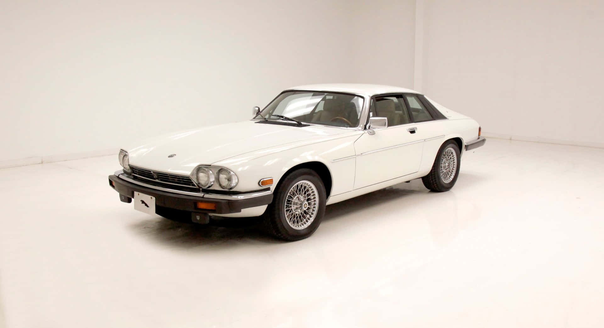 Jaguar Xjs 桌布 壁紙 — 一輛純白色的經典積架XJ-S轎跑車在明亮的攝影棚燈光下，在無縫的白色地板上閃閃發光。