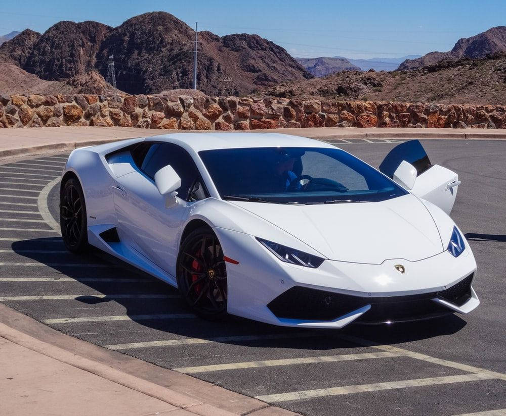 hill view 桌布 壁紙 — 一輛純白色的藍寶堅尼 Huracán 停泊在沙漠停車場，背景是崎嶇的山脈，在明亮的陽光下。