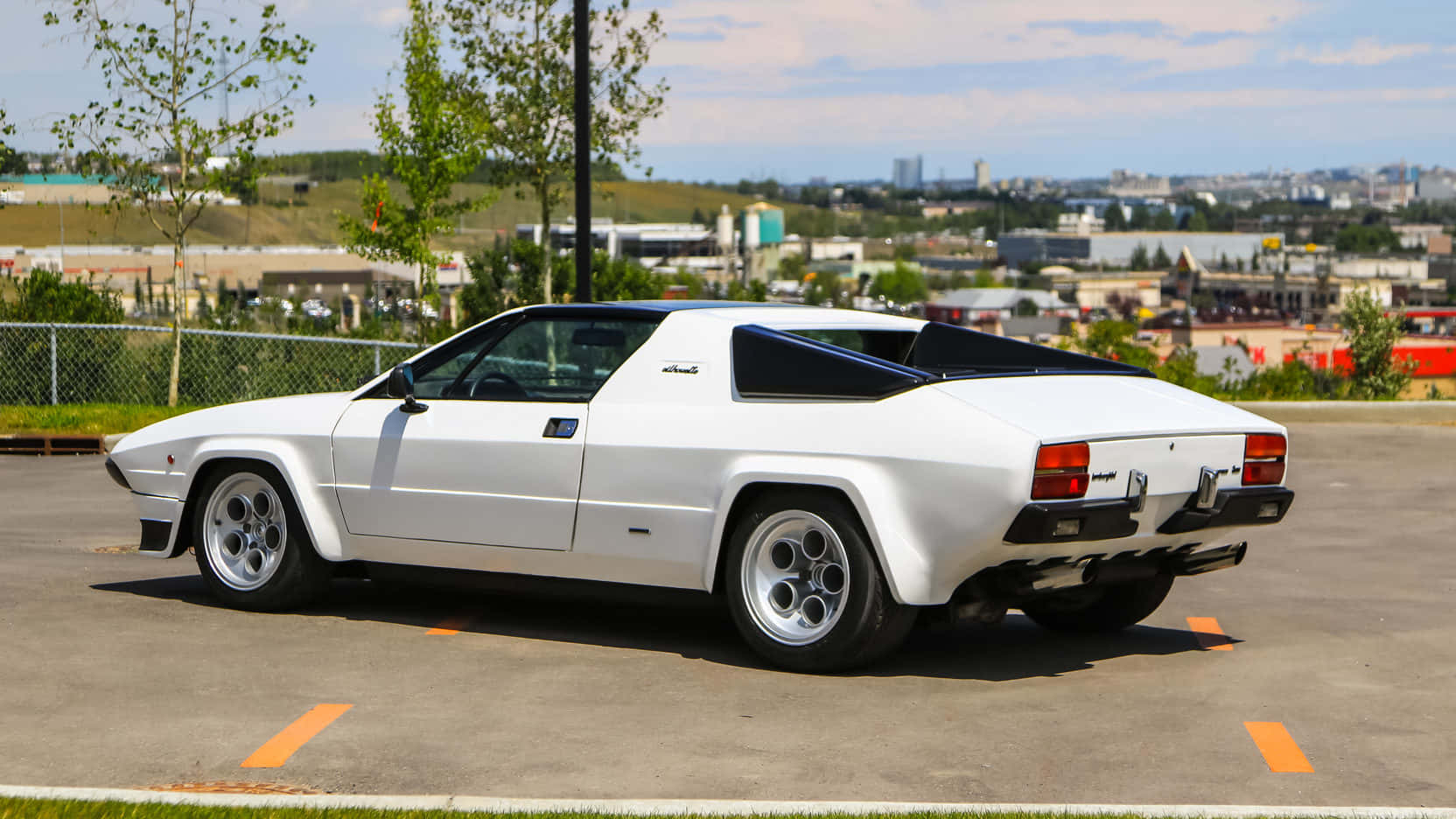 Lamborghini Silhouette 桌布 壁紙 — 一輛純白色的藍寶堅尼 Jalpa 跑車停泊在陽光普照的城市地段，背景是城市天際線。