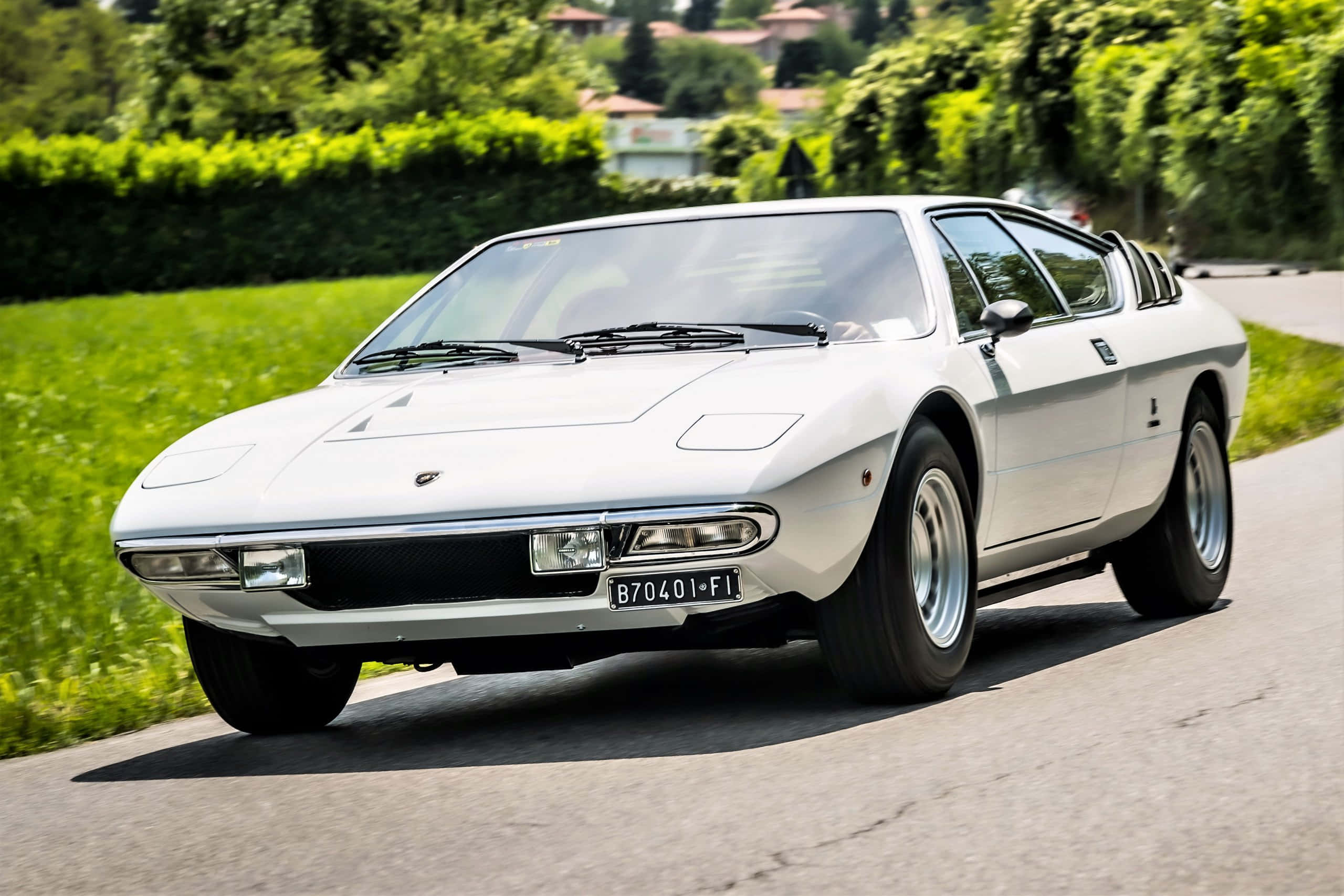 Lamborghini Urraco 桌布 壁紙 — 一輛純白色的藍寶堅尼 Marzal 在陽光明媚的鄉村道路上巡航，兩旁是茂密的綠色樹籬和樹木。