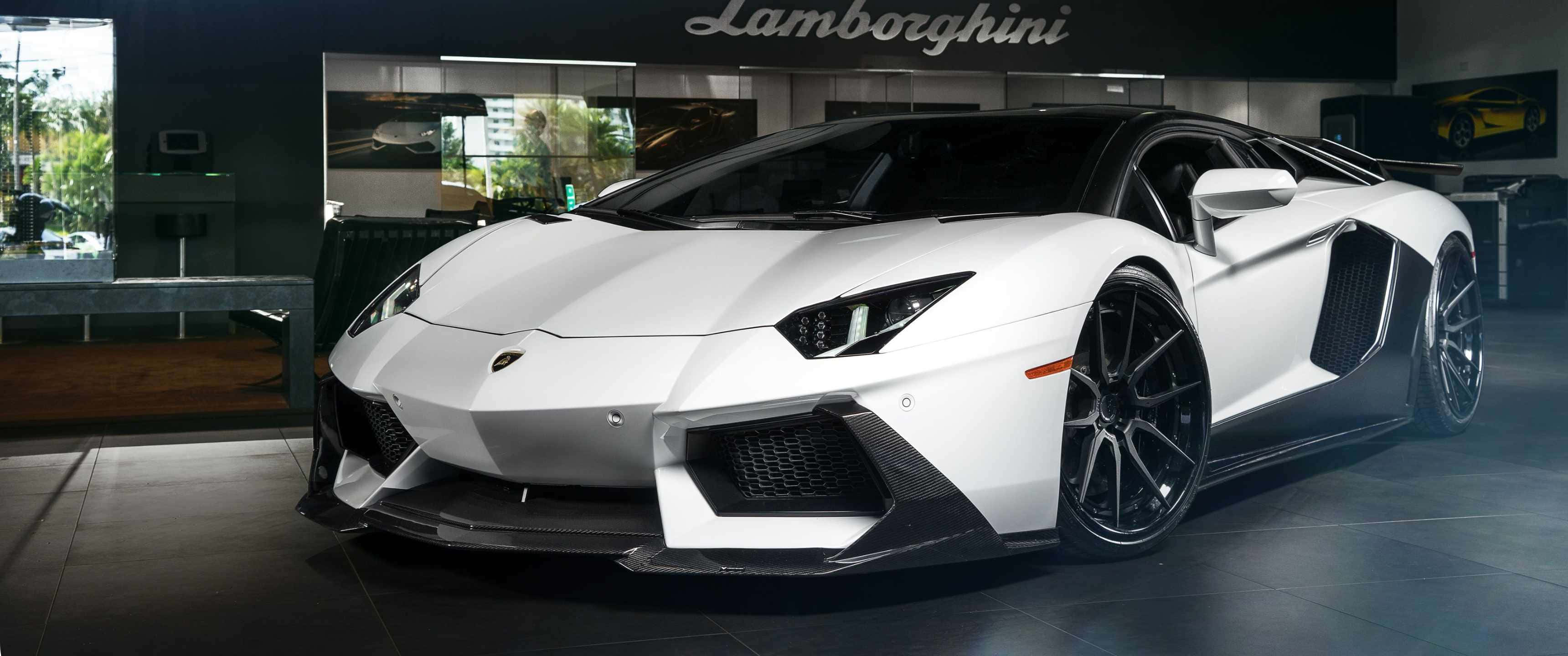 3440x1440p Lamborghini 桌布 壁紙 — 一輛純白色的藍寶堅尼Aventador跑車在展廳燈光下閃閃發光，配備黑色飾邊和定制輪圈。