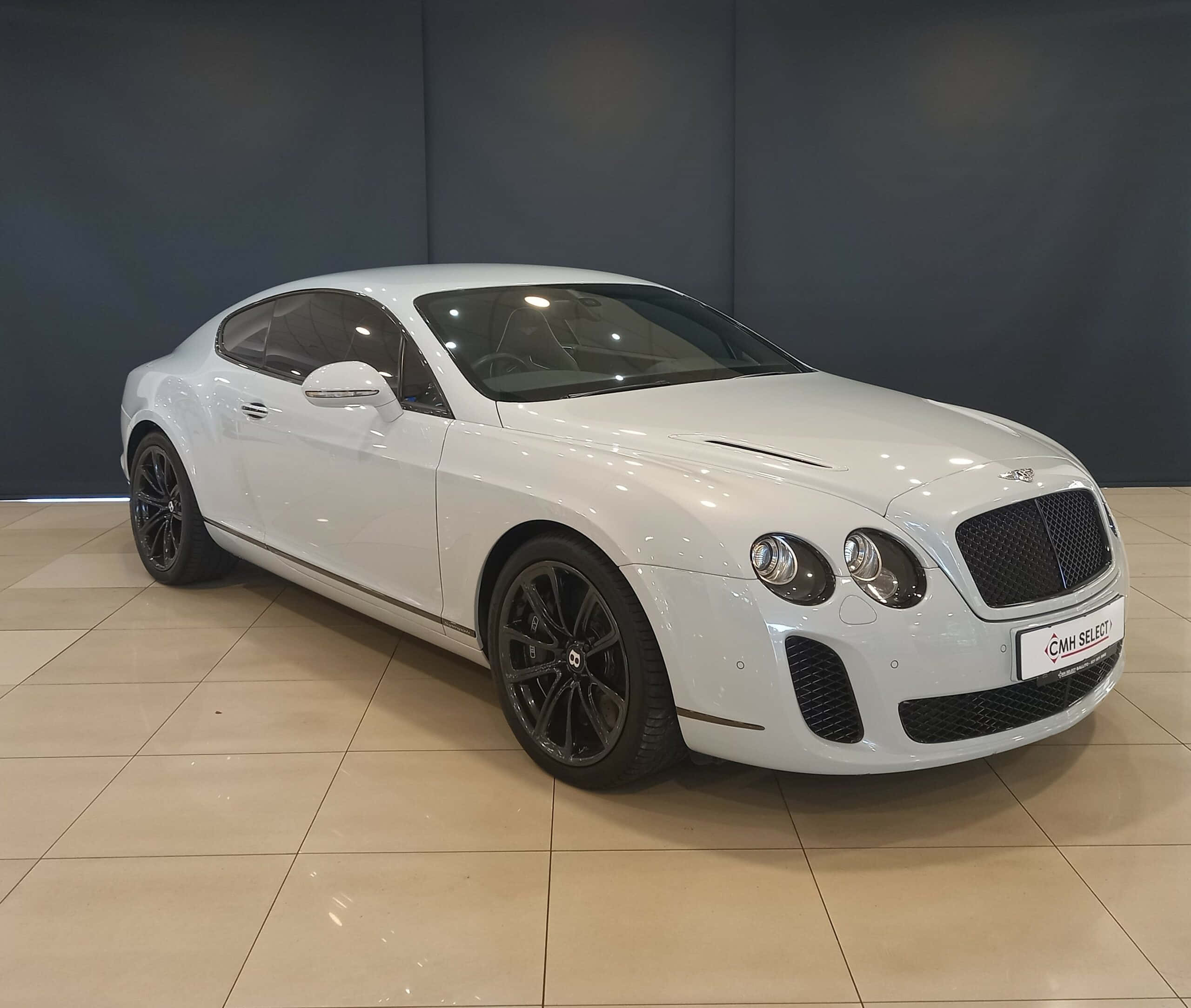 Bentley Continental Supersports 桌布 壁紙 — 一輛純白色的賓利 Continental GT 雙門轎跑車，在瓷磚地板上、深色牆壁前，於攝影棚燈光下閃閃發光。