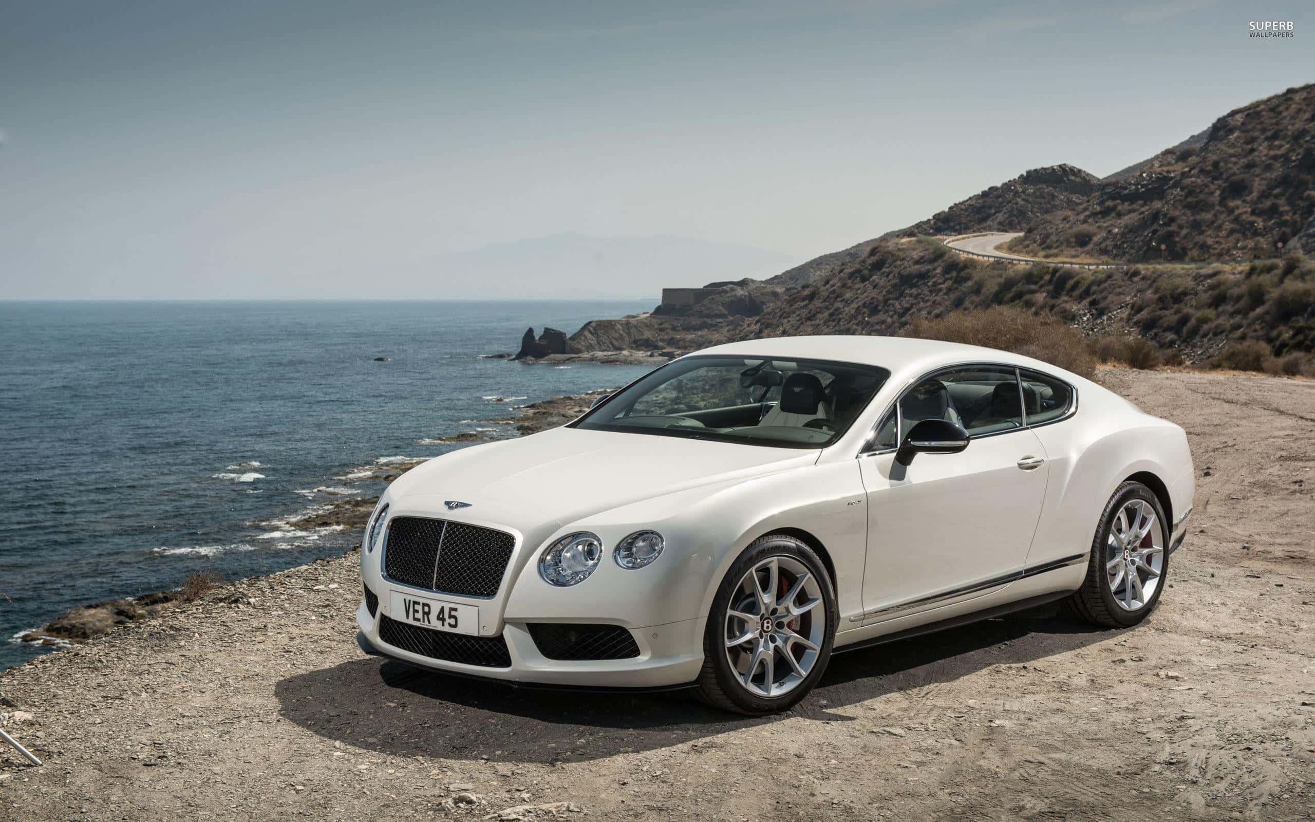 賓利 桌布 壁紙 — 一輛純白色的賓利 Continental GT 雙門轎跑車停泊在崎嶇的海岸懸崖上，俯瞰深藍色的大海。