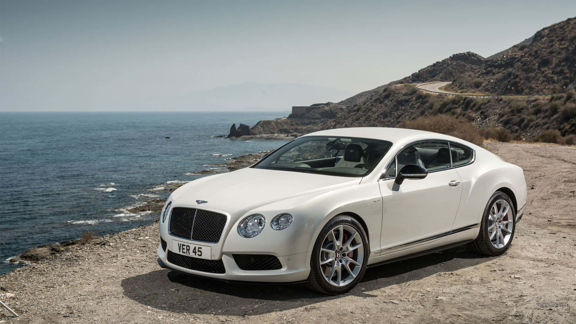 Bentley Continental Gt 桌布 壁紙 — 一輛純白色的賓利 Continental GT 停泊在崎嶇的海岸懸崖上，俯瞰深藍色的大海。