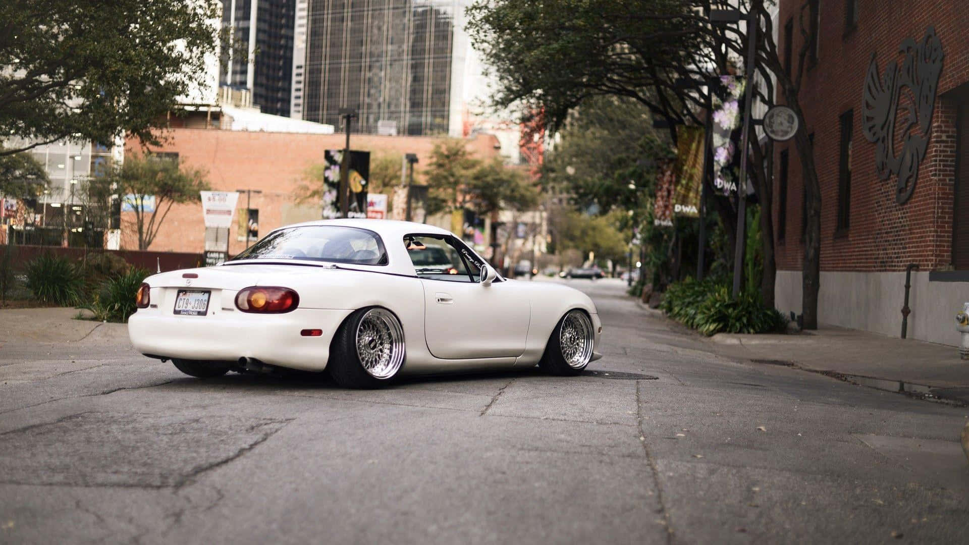 Miata 桌布 壁紙 — 一輛純白色的馬自達MX-5跑車，配備訂製輪圈，停泊在綠樹成蔭的城市街道上。