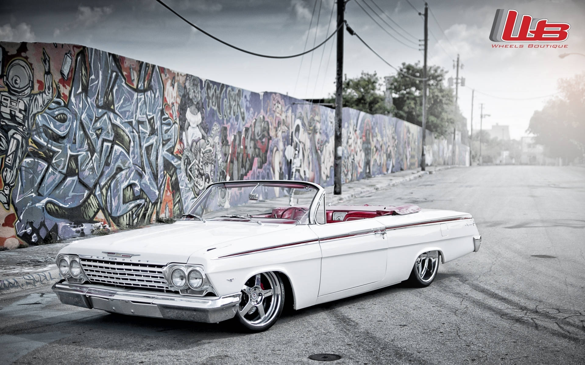 Lowrider 桌布 壁紙 — 一輛純白色經典敞篷車，紅色內裝，停放在柏油街道旁，旁邊是充滿活力的塗鴉牆。