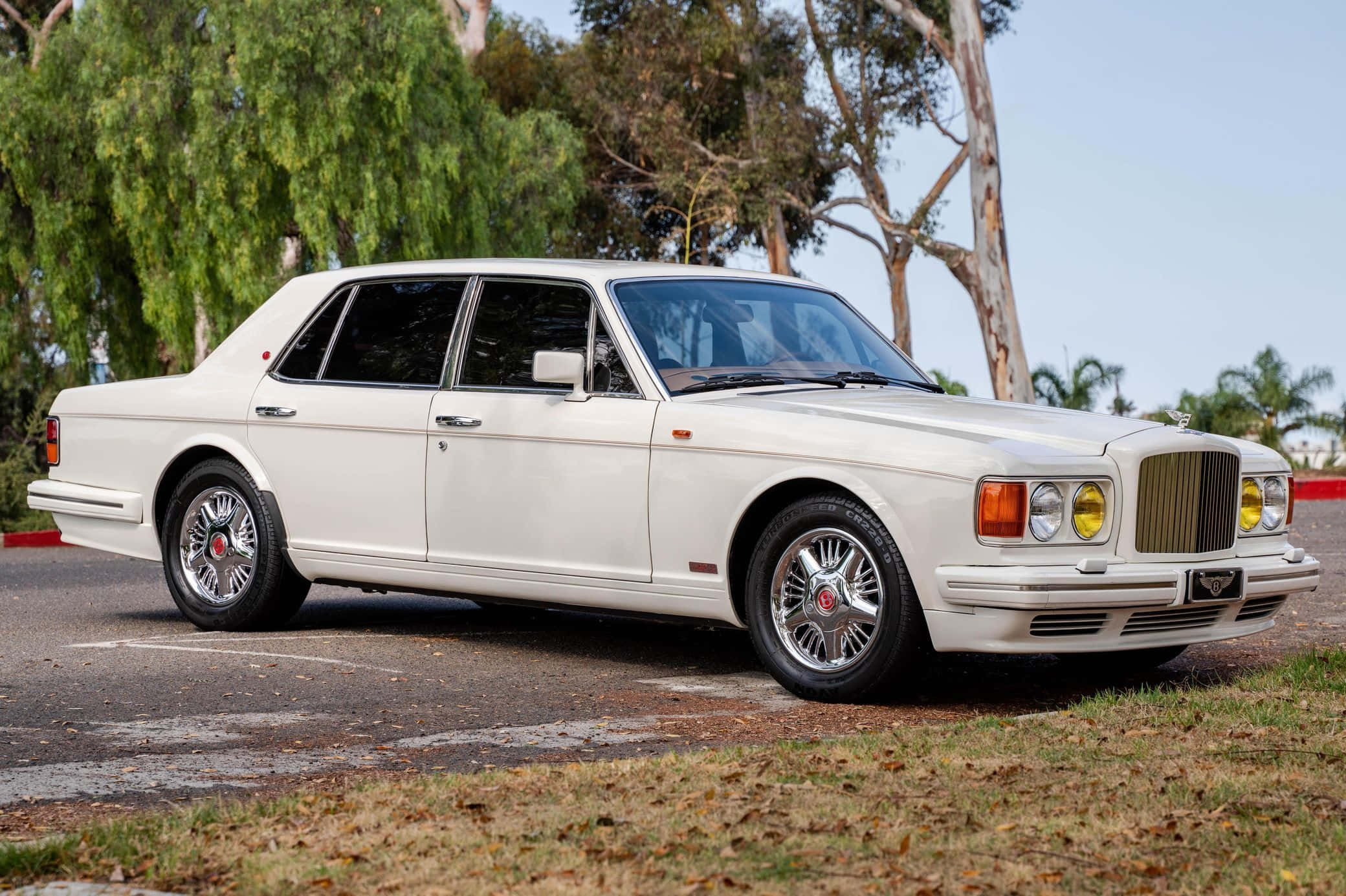 Bentley Turbo R 桌布 壁紙 — 一輛純白色賓利轎車停在柏油路上，背景有樹木和草地，天空晴朗。