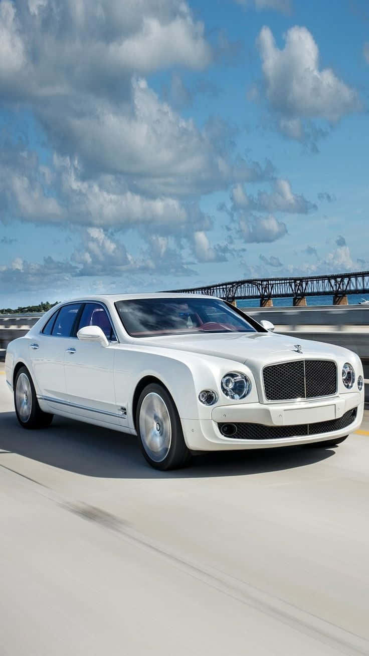 bentley HD 桌布 壁紙 — 一輛純白色賓利轎車在藍天白雲下的沿海公路巡航。
