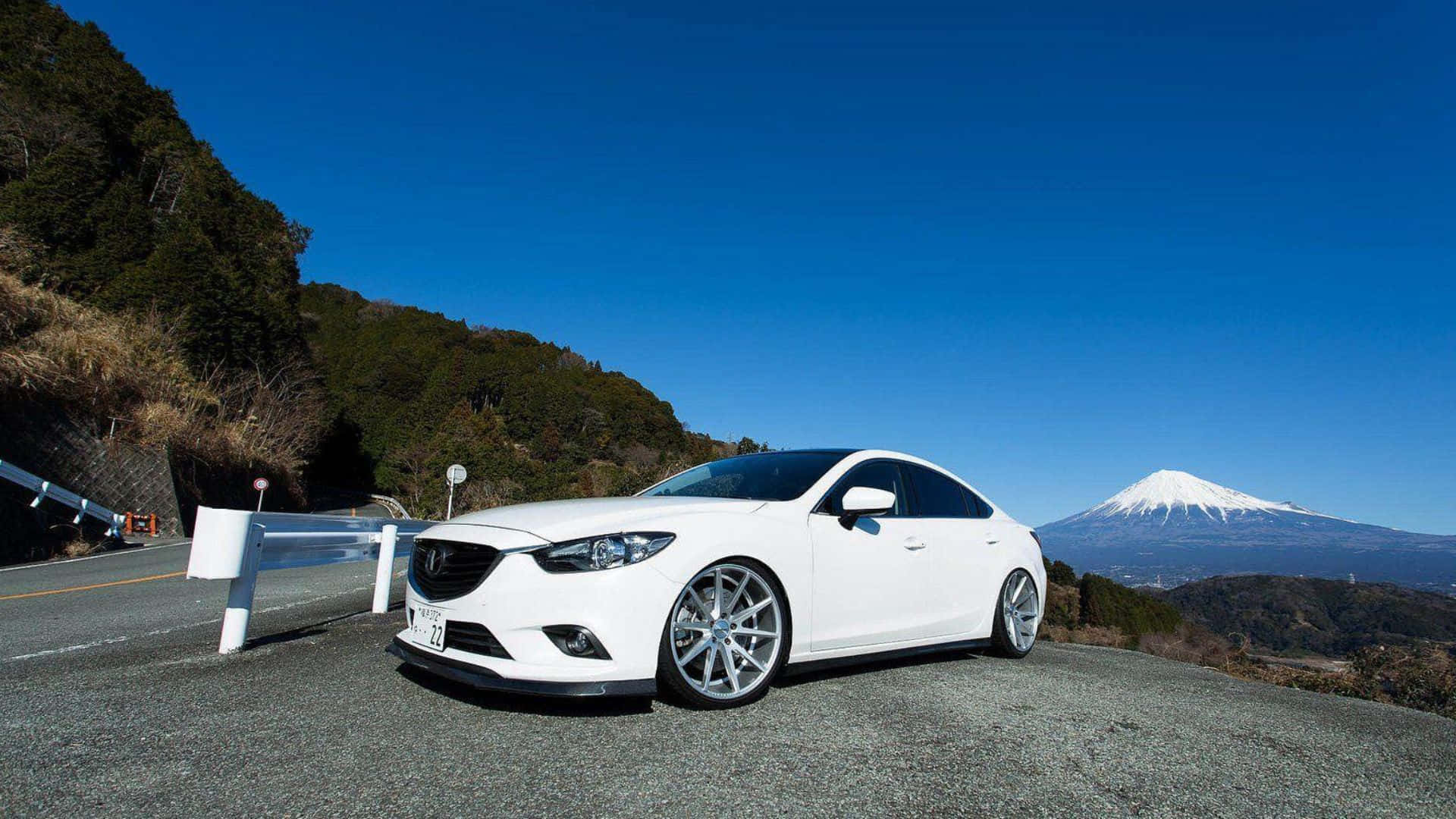 Mazda 6 桌布 壁紙 — 一輛純白色轎車停泊在山路上，白雪覆蓋的富士山在晴朗的藍天下雄偉地聳立。