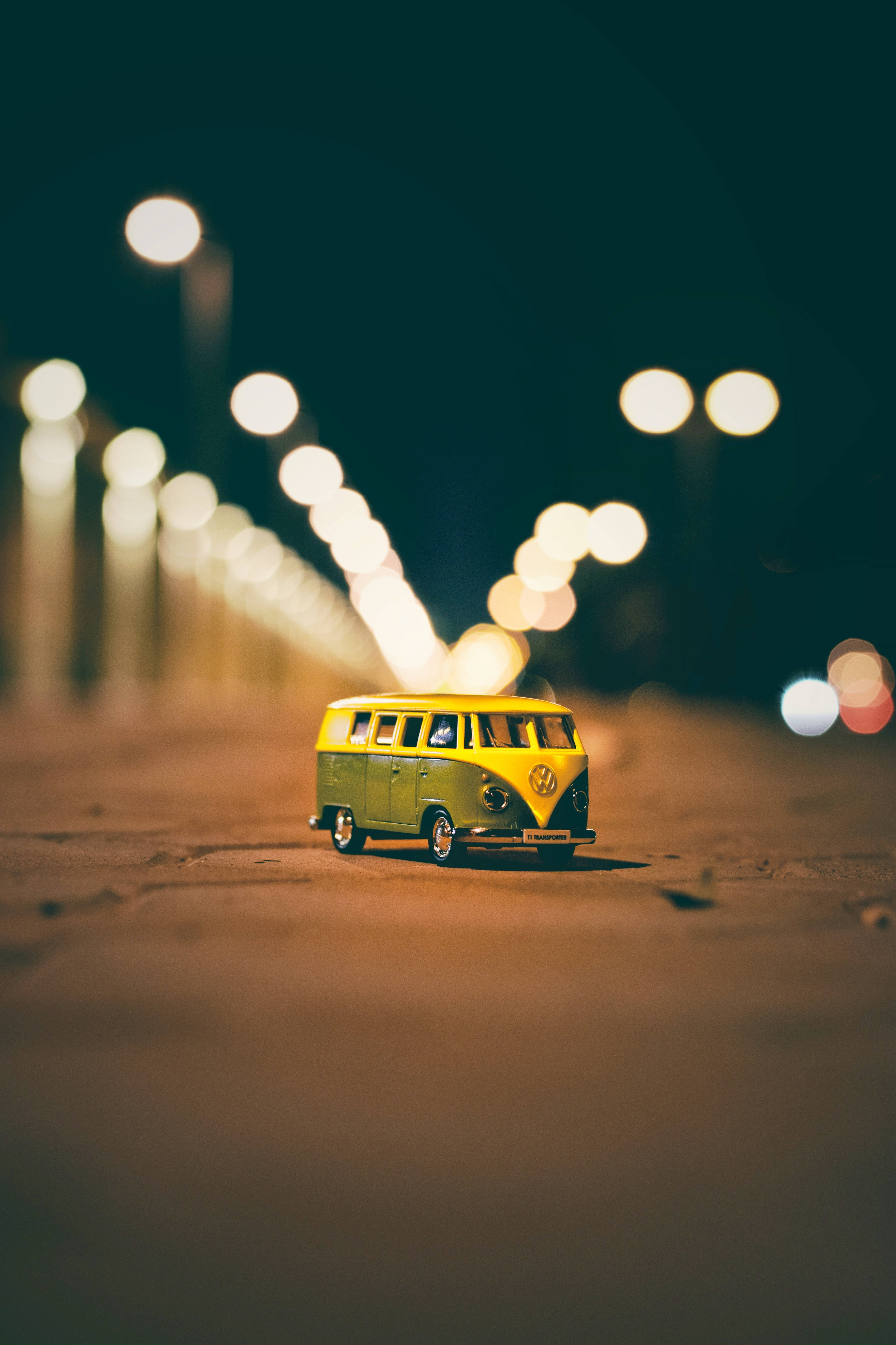Vans 桌布 壁紙 — 一輛細小的黃綠色復古廂型車在夜間停在沙地上，背景有發光的散景路燈。