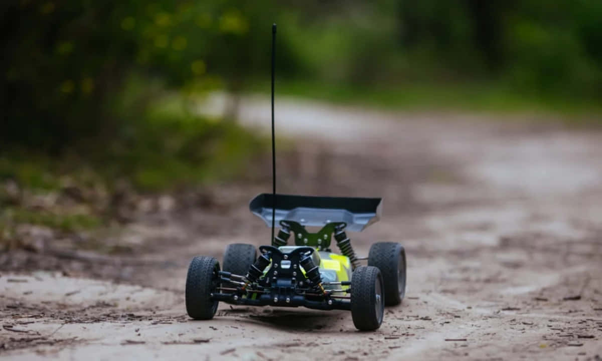 Rc Cars 桌布 壁紙 — 一輛細節豐富的遙控車，帶有外露的懸掛系統和天線，停在被模糊綠色樹葉包圍的泥土小徑上。