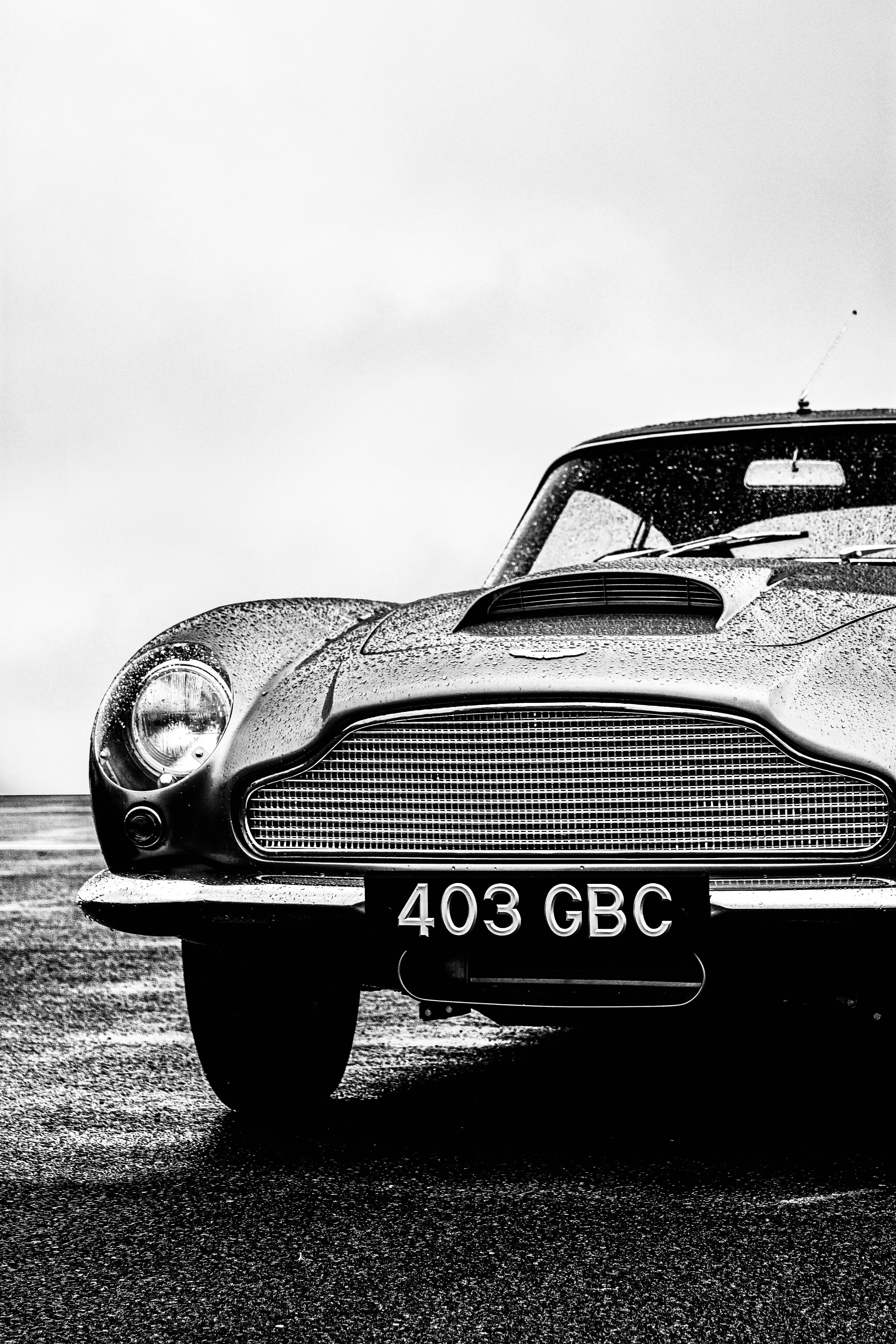 復古 桌布 壁紙 — 一輛經典 Aston Martin 的黑白特寫，雨滴在鍍鉻格柵和引擎蓋上閃閃發光。