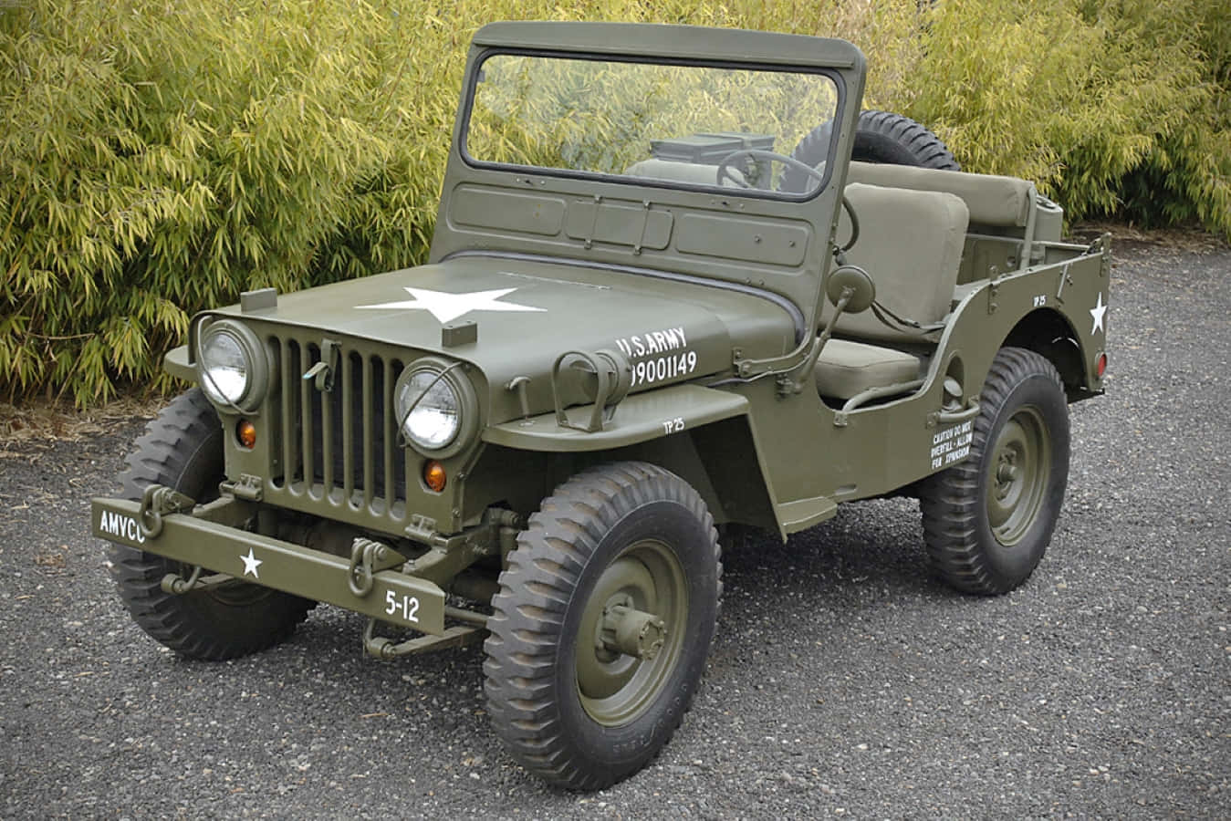 Jeep Willys 桌布 壁紙 — 一輛經典橄欖綠色的美國陸軍吉普車，帶有白色星星和標記，停在碎石地上，旁邊是茂密的竹子。