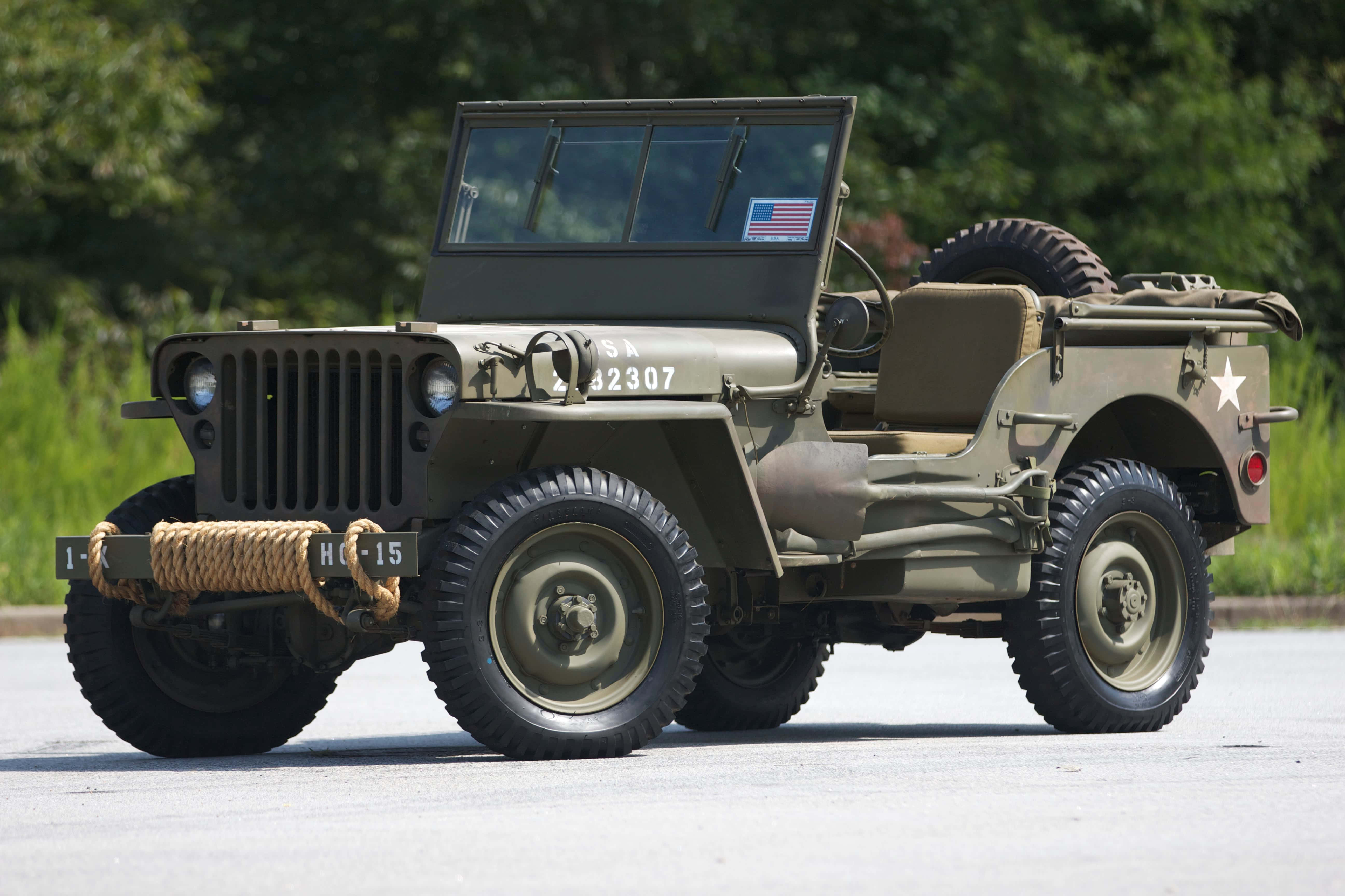 Jeep Willys 桌布 壁紙 — 一輛經典橄欖綠軍用吉普車，帶有星形徽章和繩索保險桿，在明亮的日光下停在路面上。