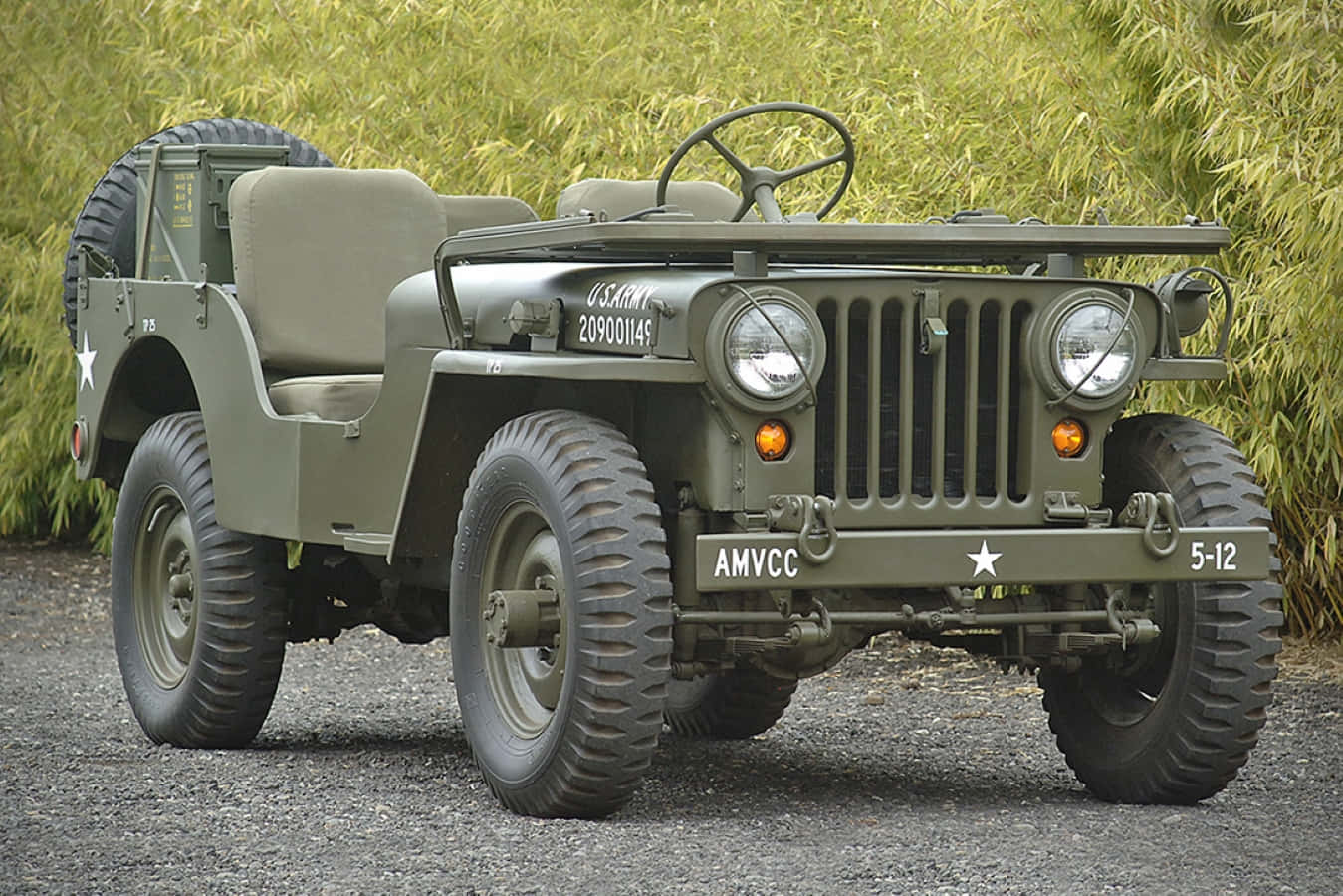 Jeep Willys 桌布 壁紙 — 一輛經典橄欖綠軍用吉普車帶有星形徽章，停在碎石地上，旁邊是高高的草叢。
