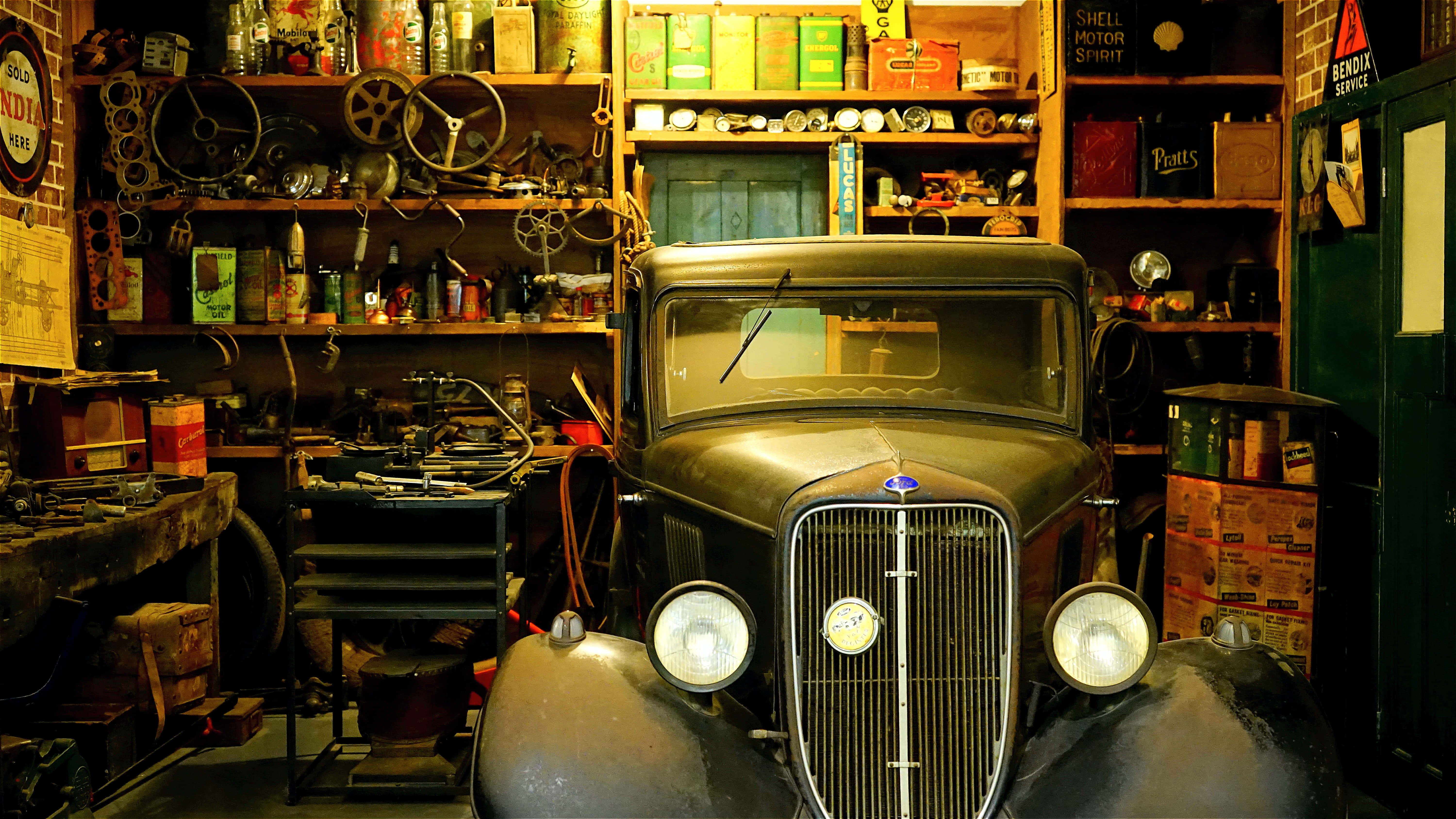 Mechanical Engineering 桌布 壁紙 — 一輛經典汽車在溫暖燈光下閃耀，車庫雜亂無章，充滿了經典汽車紀念品和工具。