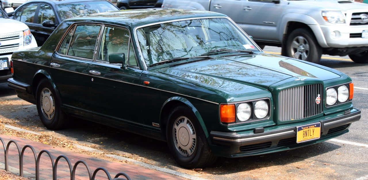 Bentley Turbo R 桌布 壁紙 — 一輛經典深綠色賓利房車停泊在散落著秋葉的城市街道上。