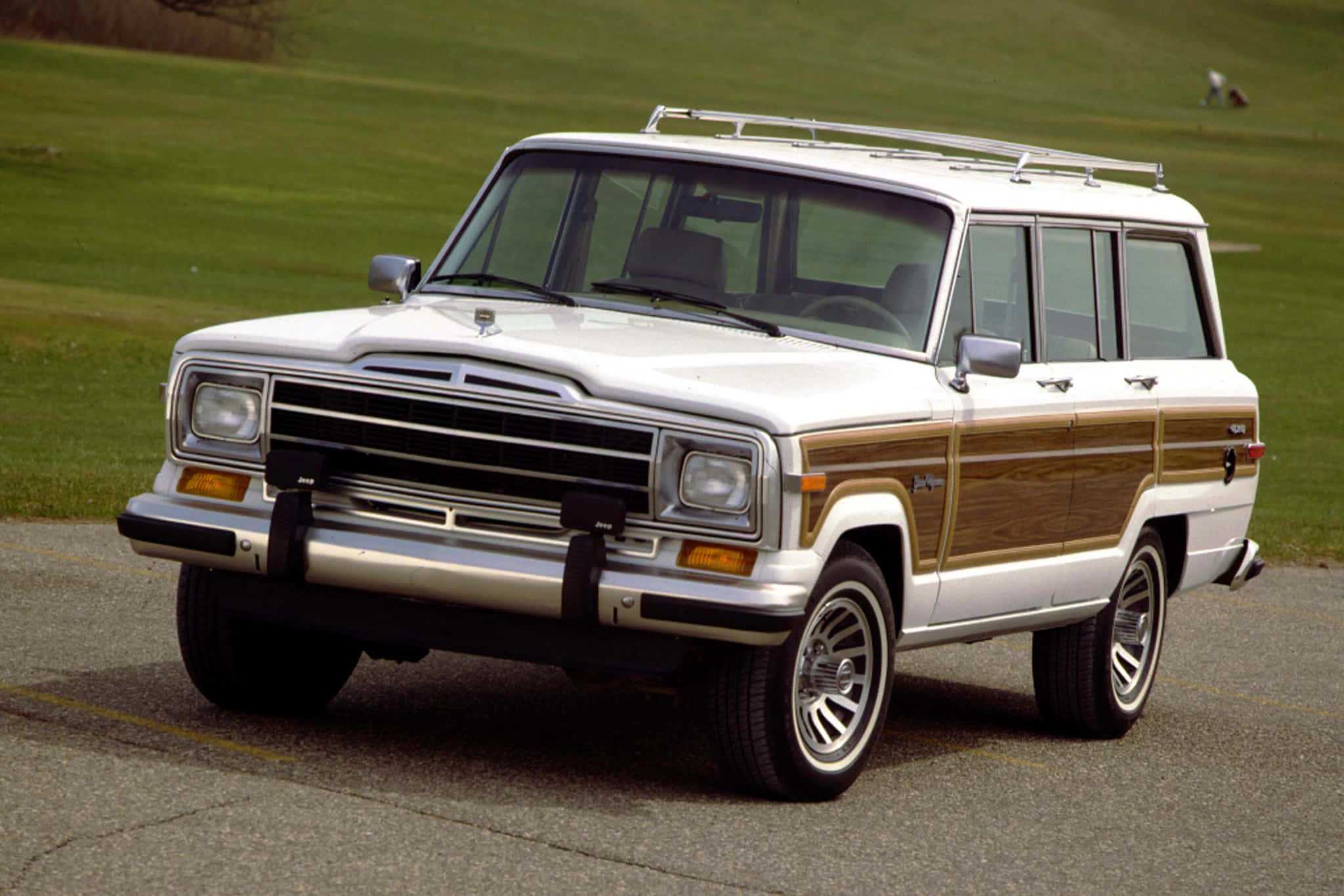 Jeep Wagoneer 桌布 壁紙 — 一輛經典白色Jeep Wagoneer配木紋飾板，停泊在鋪砌道路上，背景是綠色草地。