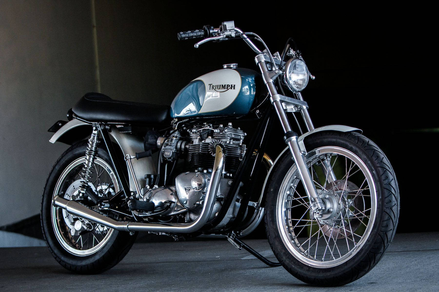 Triumph 桌布 壁紙 — 一輛經典的Triumph摩托車，帶有鍍鉻細節和藍銀色油箱，在黑暗的攝影棚背景下蓄勢待發。