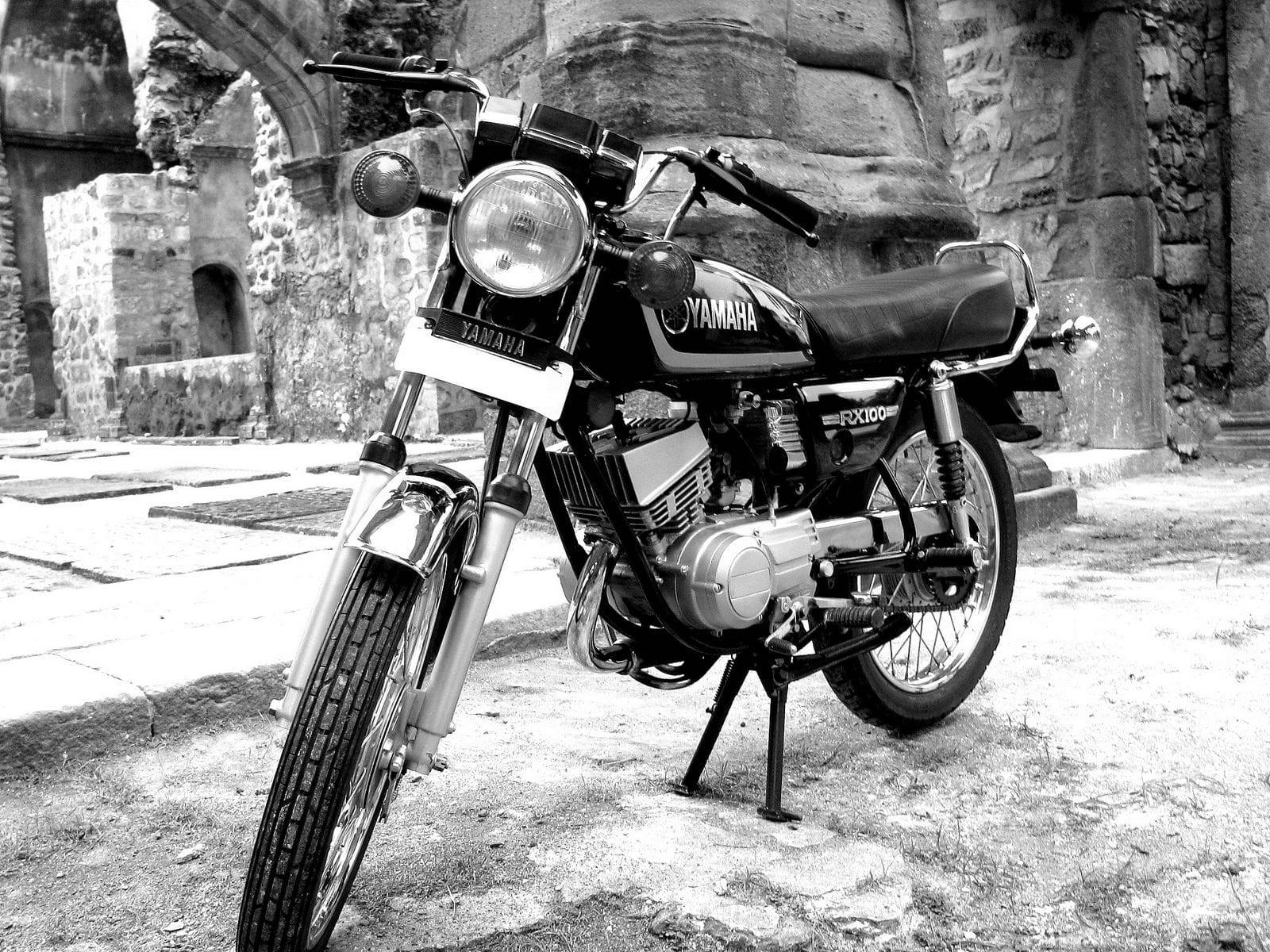 Rx100 桌布 壁紙 — 一輛經典的Yamaha FX100機車以黑白風格矗立在古代廢墟拱門中的石座上。