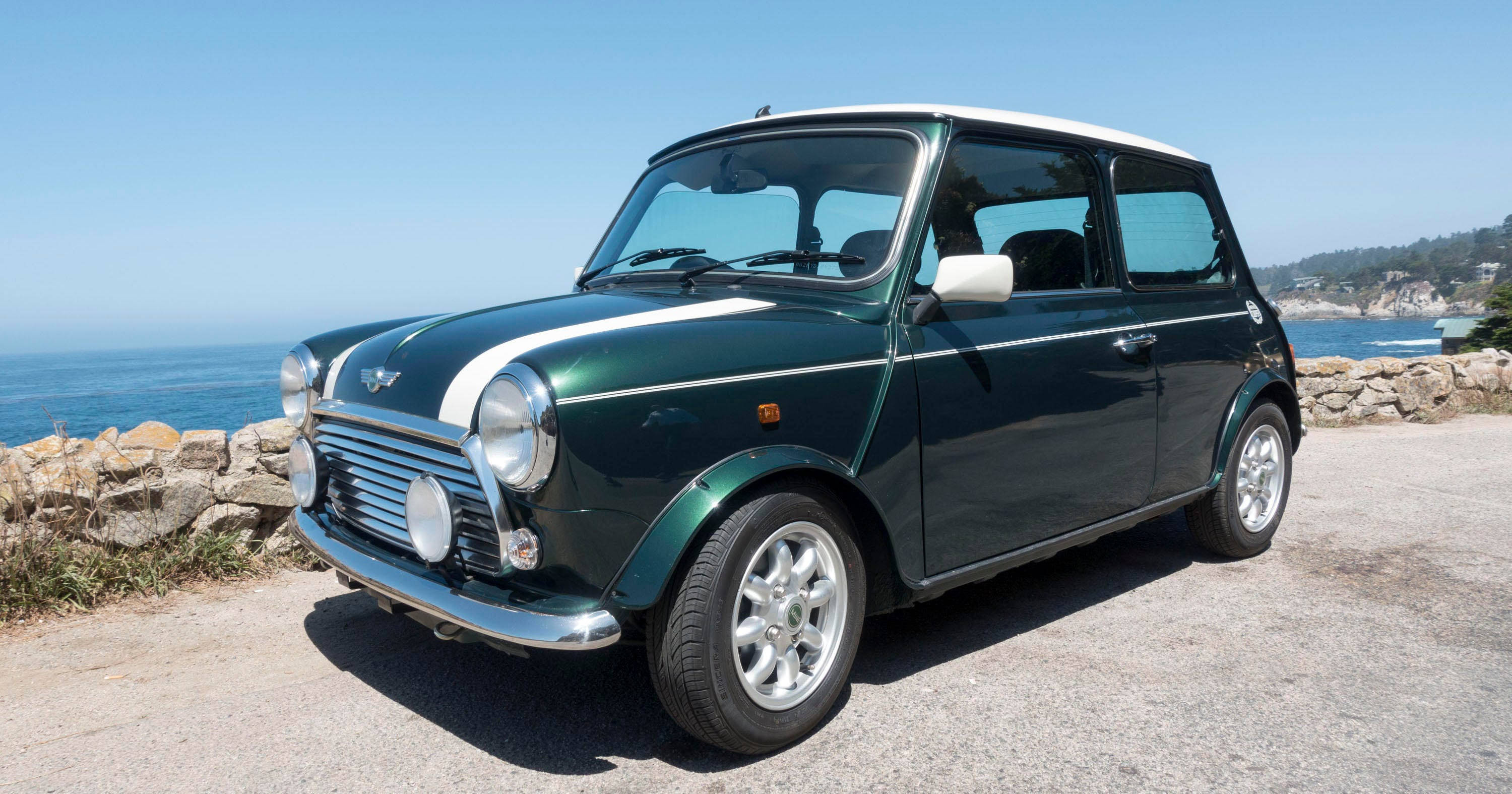海洋 桌布 壁紙 — 一輛經典的綠色Mini Cooper，白色車頂和賽車條紋，停在沿海公路上，俯瞰海洋，天空清澈湛藍。