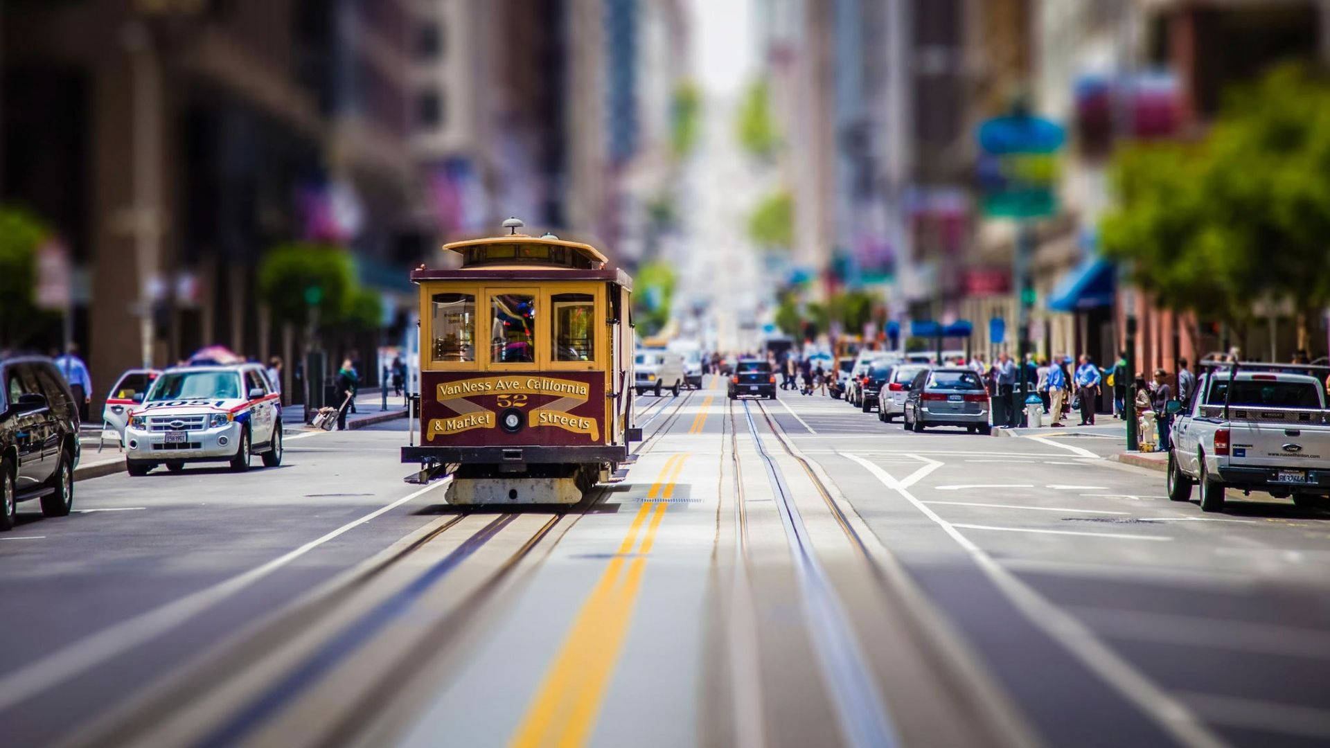 Road 桌布 壁紙 — 一輛經典的舊金山纜車在繁忙的城市街道上行駛，背景是模糊的汽車和行人。