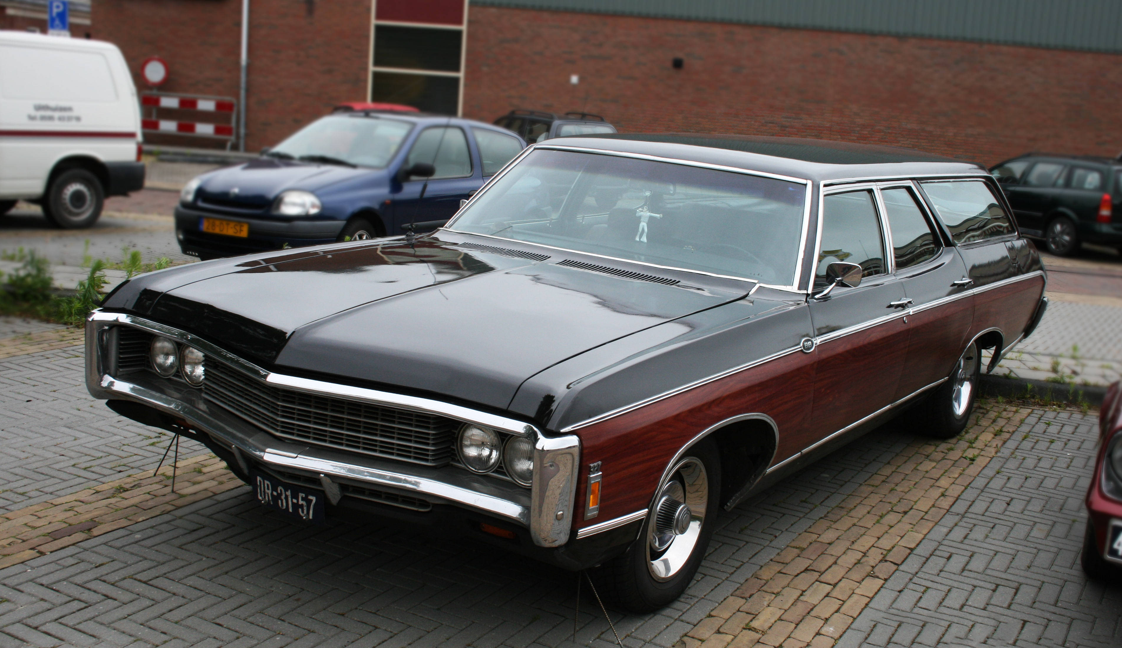 chevrolet impala 1967 桌布 壁紙 — 一輛經典的雙色旅行車，黑色和栗色車漆在日光下閃閃發光，停在磚砌停車場上。