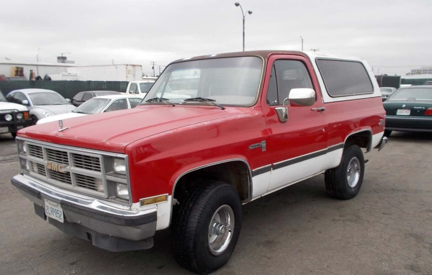 Gmc Jimmy 桌布 壁紙 — 一輛經典紅白GMC皮卡車停放在多雲的戶外停車場，附近有其他車輛。