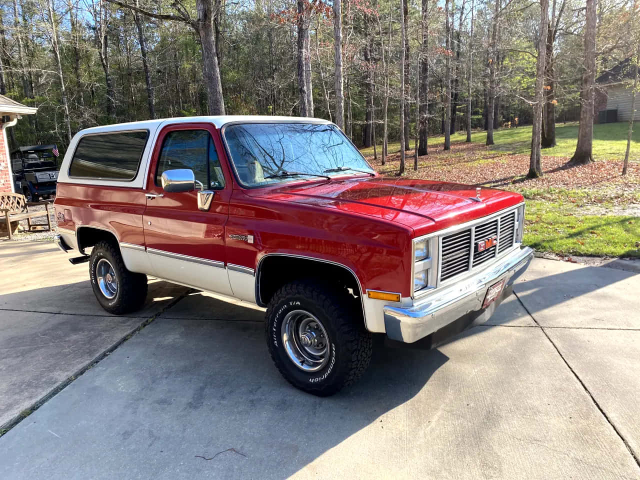 Gmc Jimmy 桌布 壁紙 — 一輛經典紅白色GMC皮卡車，帶有鍍鉻裝飾，停在混凝土車道上，周圍是光禿禿的樹木和落葉。