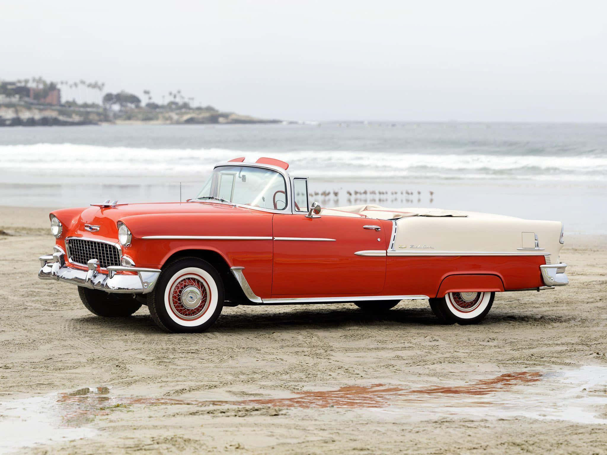 chevy 桌布 壁紙 — 一輛經典紅白色敞篷車停在濕沙灘上，背景有海浪和遠處的懸崖。