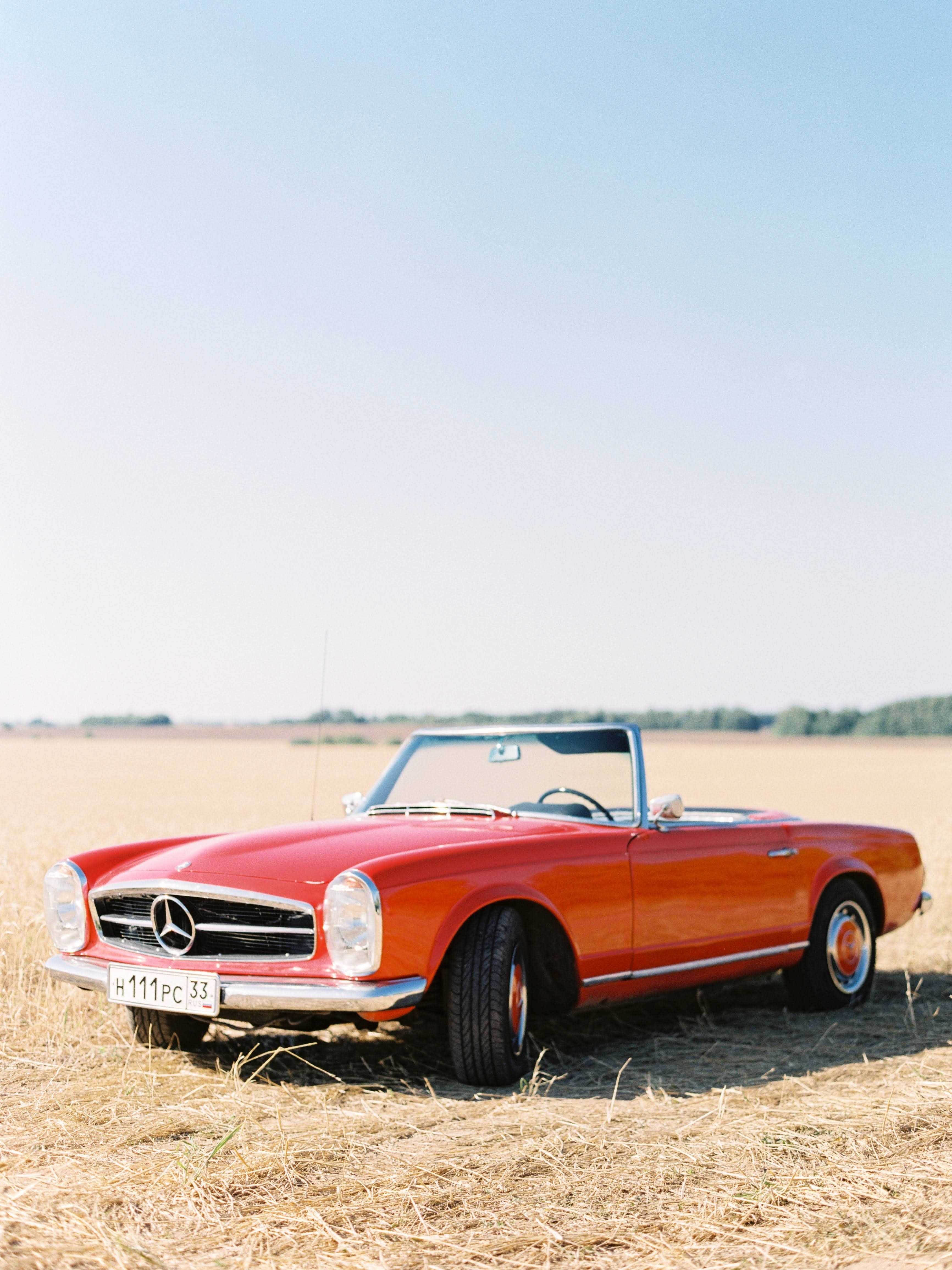 mercedes amg iPhone 桌布 壁紙 — 一輛經典紅色梅賽德斯-奔馳敞篷車停放在金色麥田中，上方是清澈的藍天。