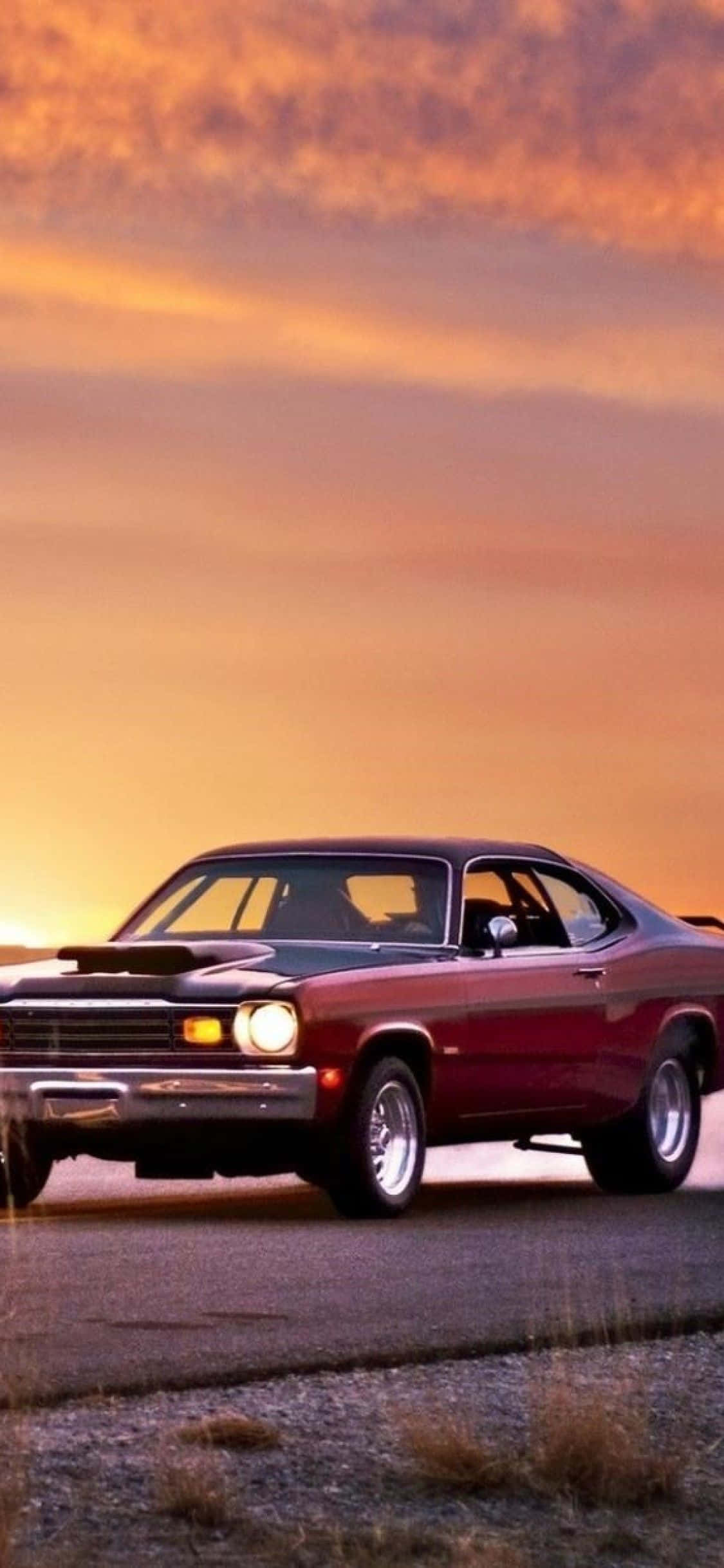 Vintage Car iPhone 桌布 壁紙 — 一輛經典紅色肌肉車停泊在碎石路邊，天空是火熱的橙色日落。