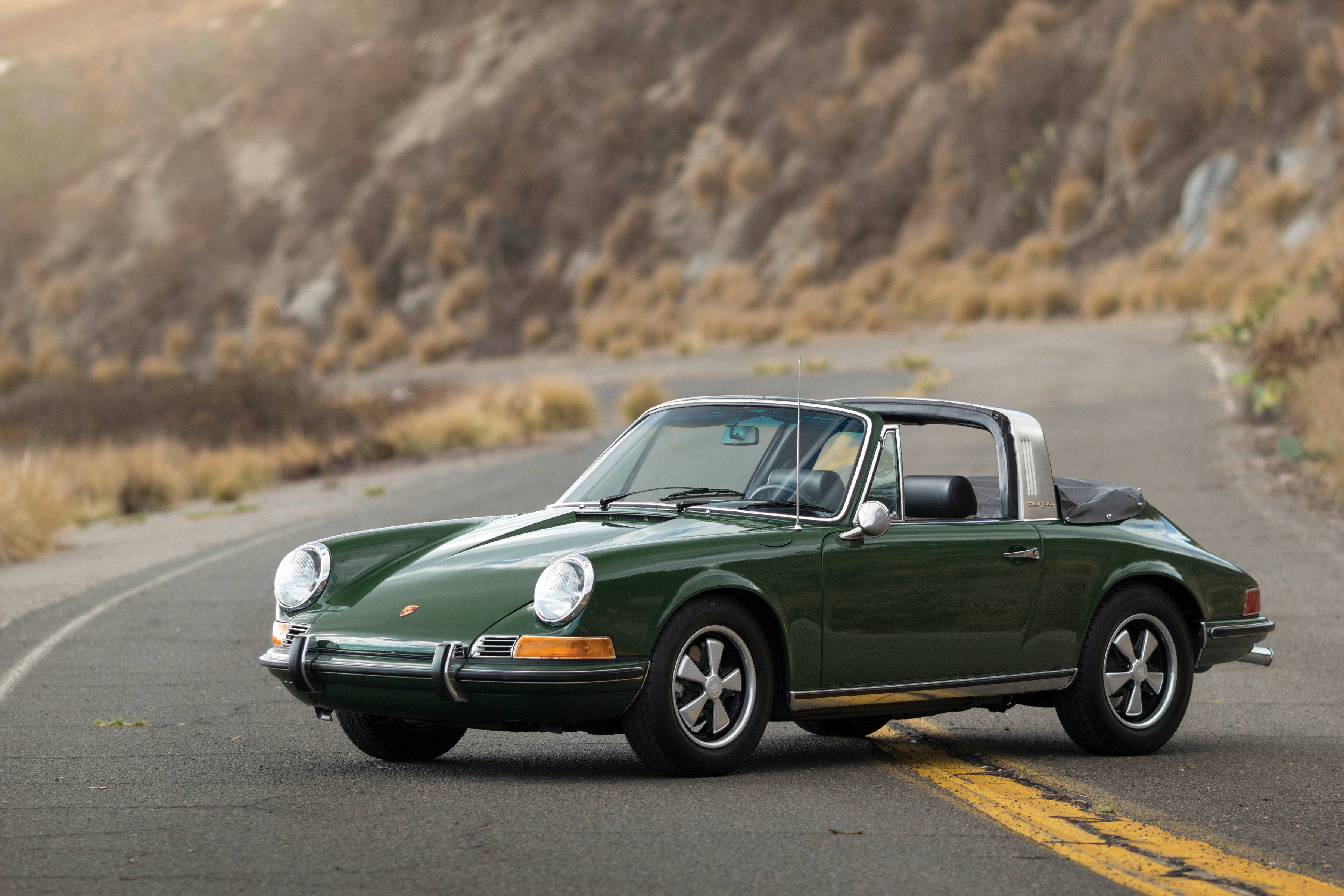 Porsche 911 桌布 壁紙 — 一輛經典綠色保時捷912T敞篷車沿著蜿蜒的山路行駛，兩旁是乾燥的草坡，沐浴在柔和的金色光線下。