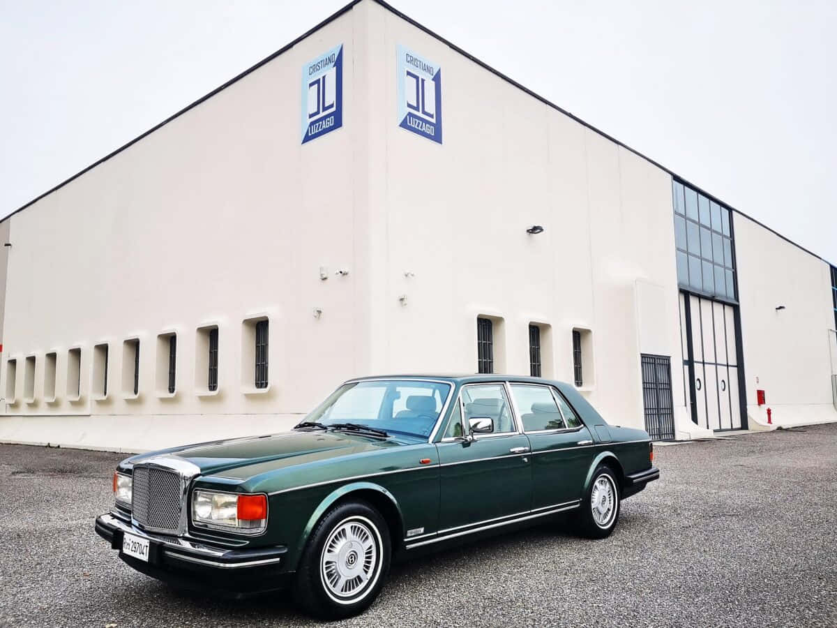 Bentley Eight 桌布 壁紙 — 一輛經典綠色賓利轎車停在一棟帶有藍色標誌的現代白色工業建築前。