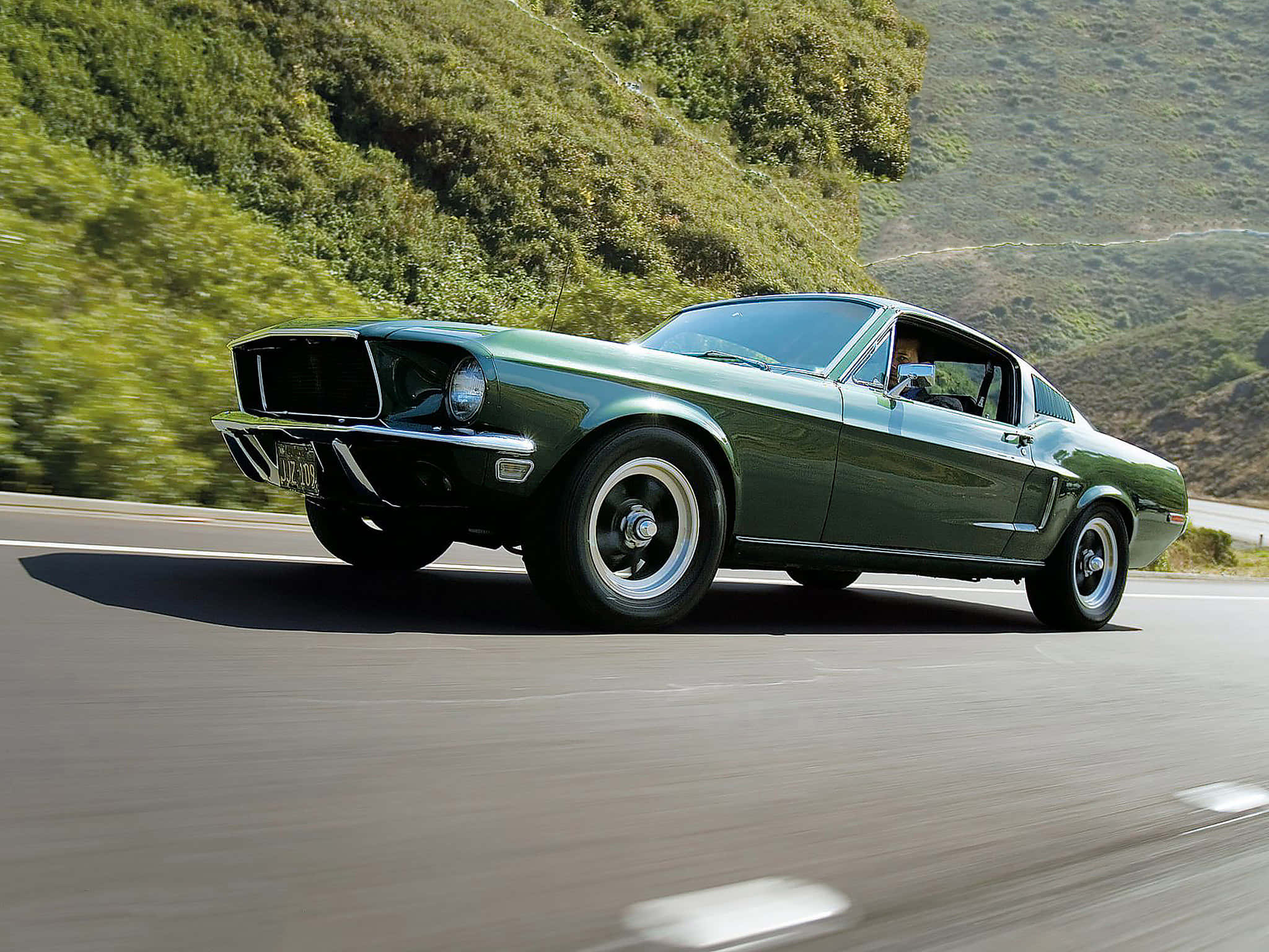 Ford Mustang 桌布 壁紙 — 一輛經典綠色野馬跑車沿著蜿蜒的山路行駛，兩旁翠綠的山坡飛掠而過。