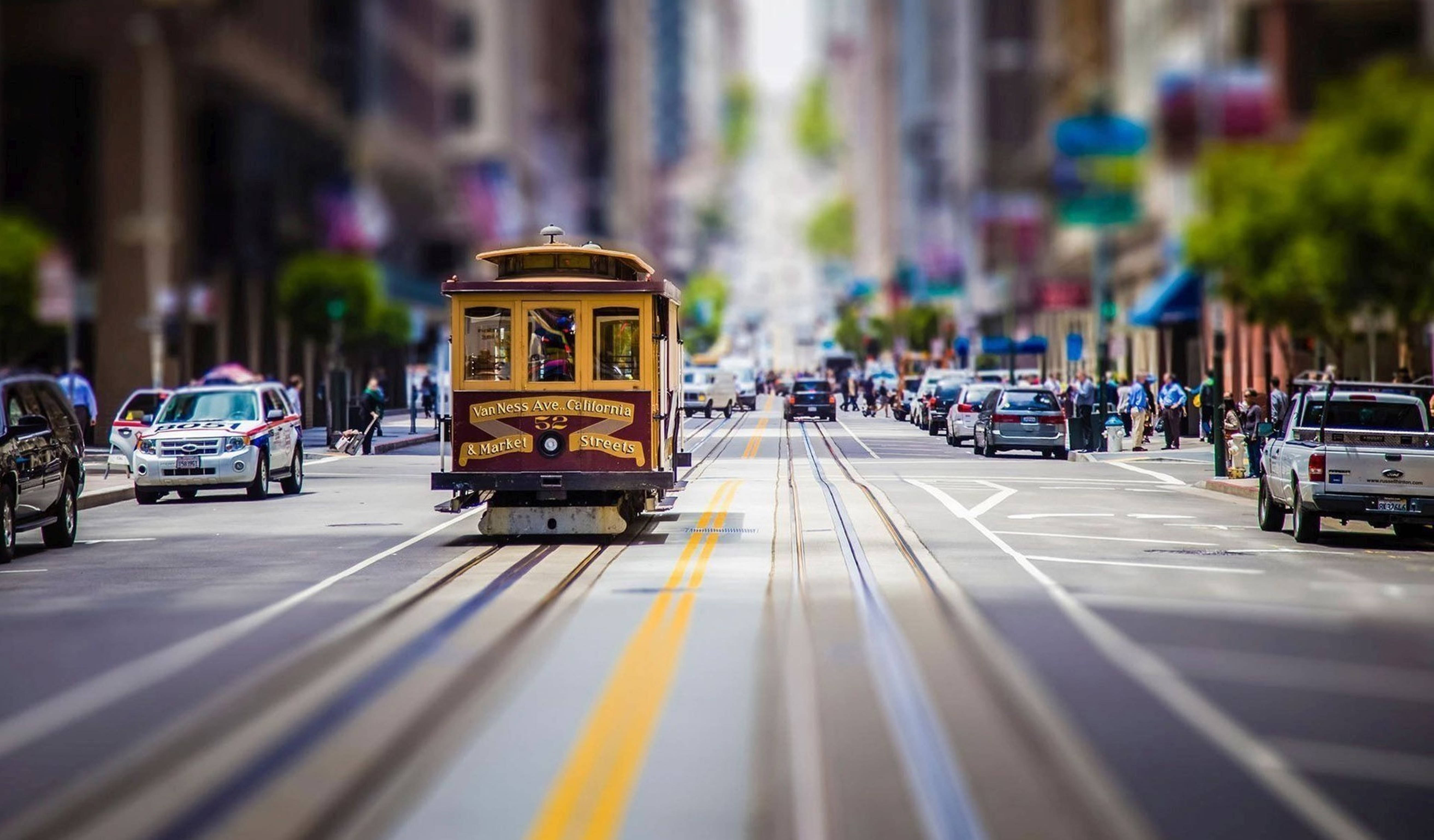 城市風景 桌布 壁紙 — 一輛經典纜車沿著繁華的城市街道滑行，帶有模糊的動感和充滿活力的都市能量。