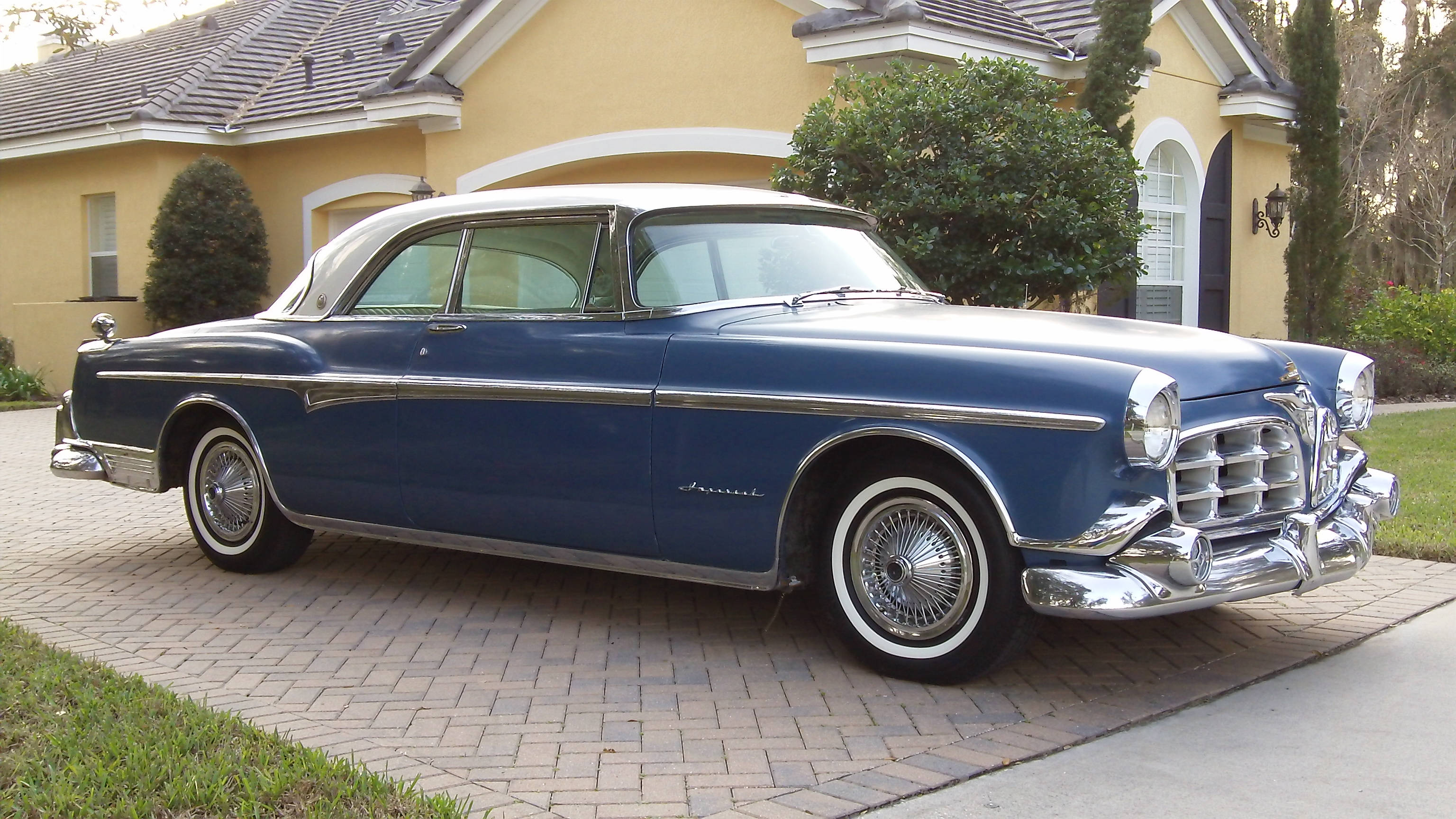 Chrysler 桌布 壁紙 — 一輛經典藍白色1950年代轎車在日光下閃耀，停放在黃色房屋前的磚砌車道上。
