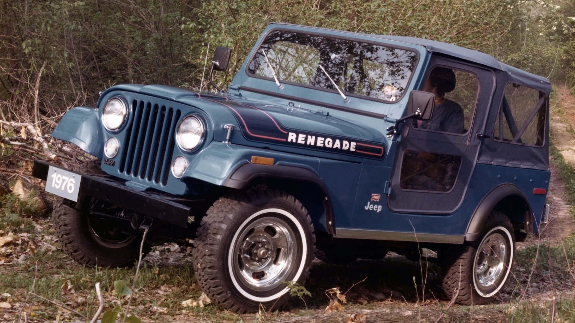 Jeep Cj 桌布 壁紙 — 一輛經典藍色1976年Jeep Renegade在森林小徑上堅固地站立，輪胎緊抓泥土和草地。
