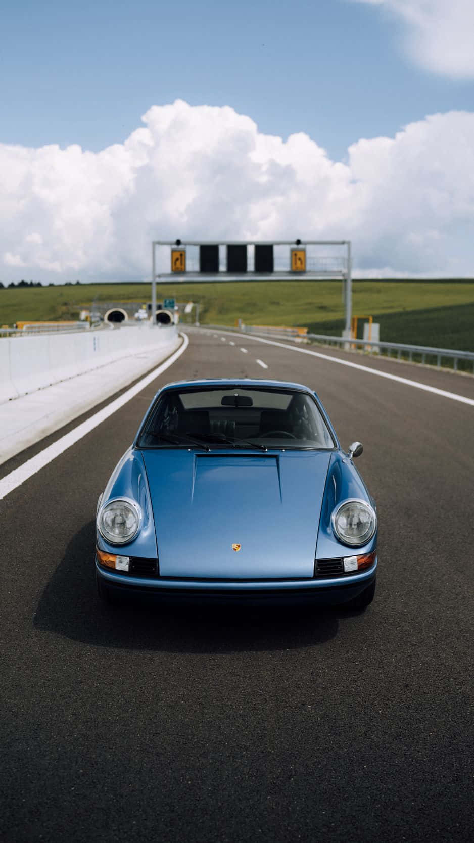 Porsche iPhone 桌布 壁紙 — 一輛經典藍色保時捷911在戲劇性的多雲天空下，在陽光明媚的高速公路上疾馳。