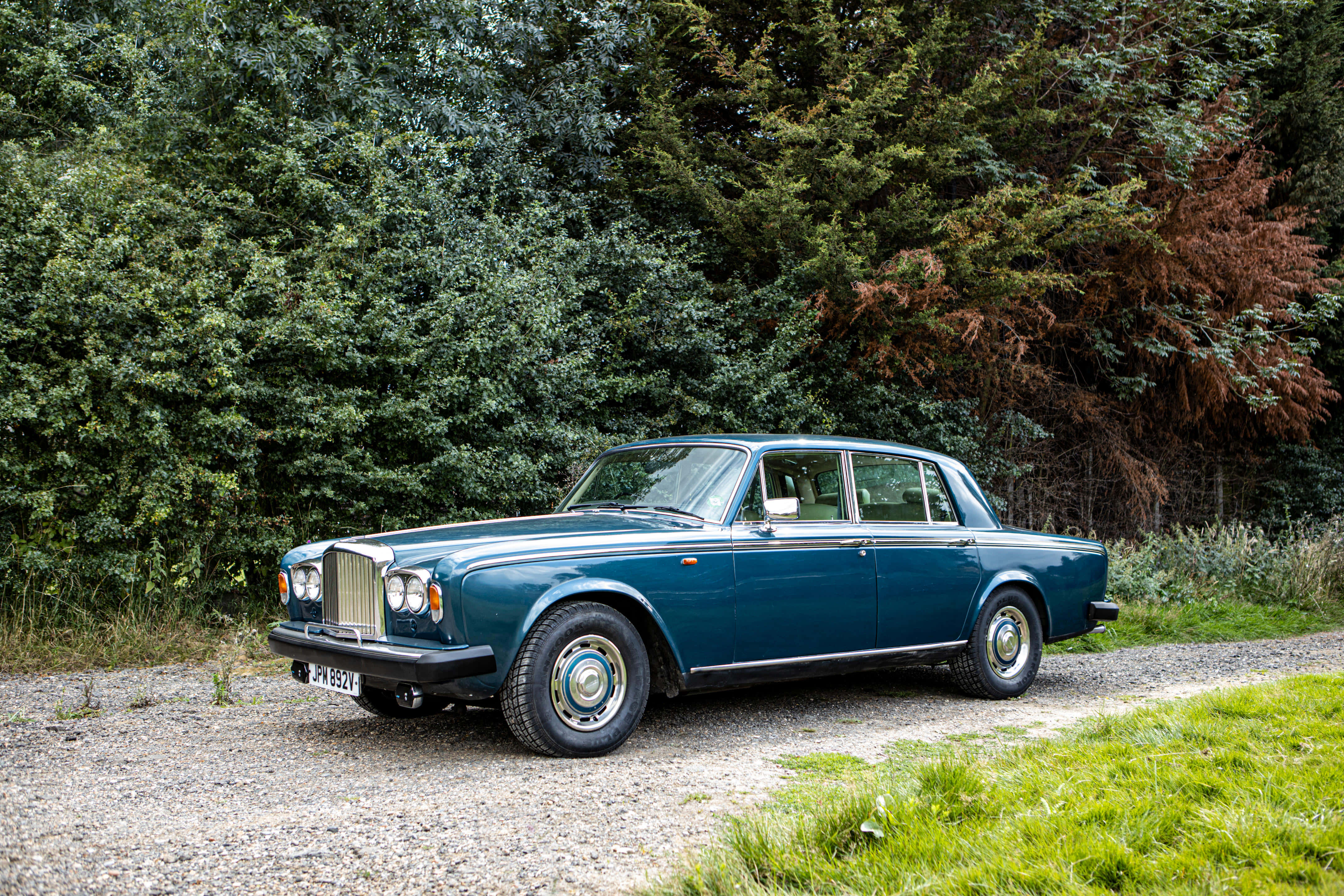 Bentley T2 桌布 壁紙 — 一輛經典藍色勞斯萊斯銀影停泊在碎石路上，旁邊是茂密的綠樹和草地。