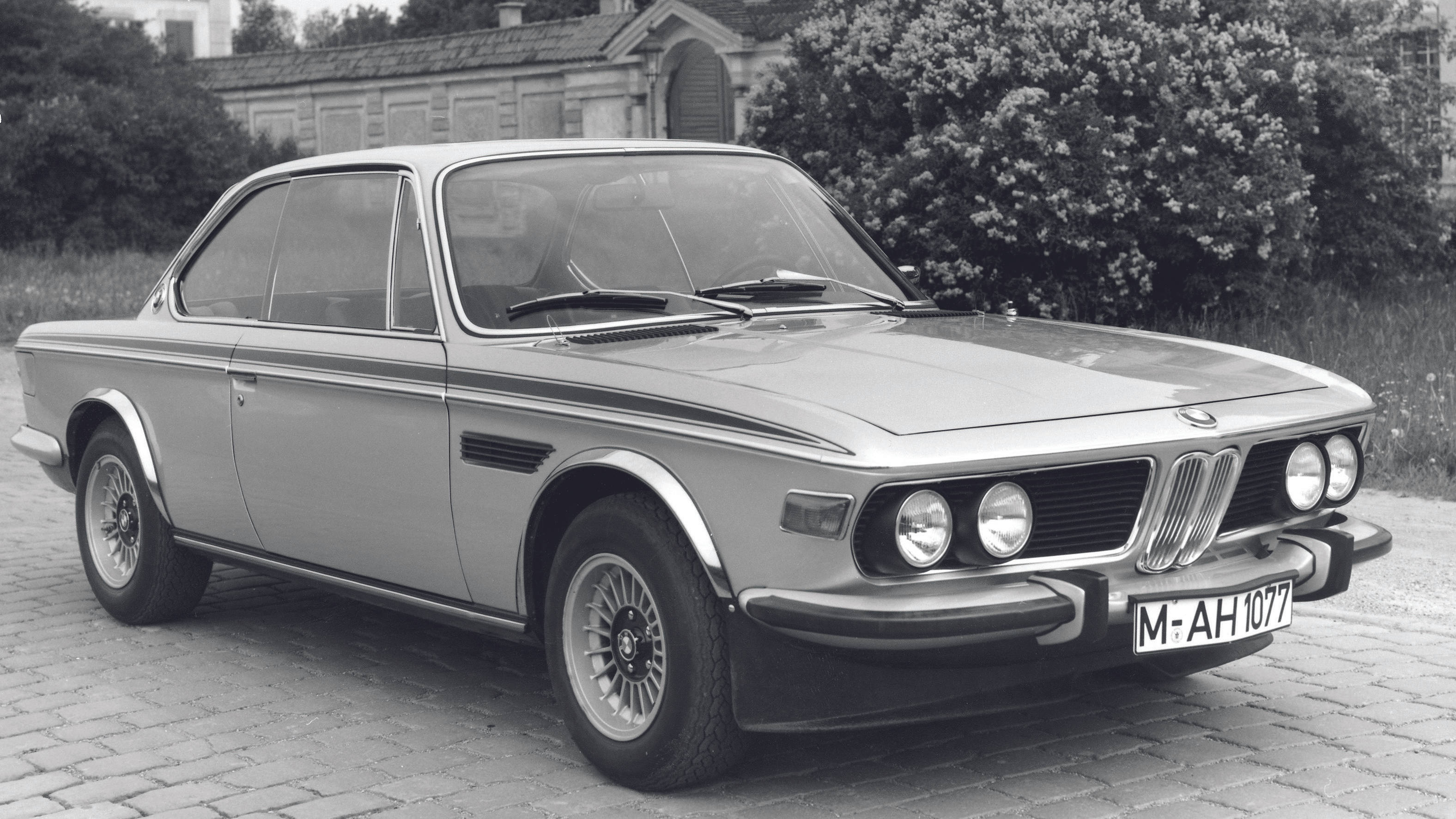 classic bmw 桌布 壁紙 — 一輛經典銀色寶馬雙門轎跑車停泊在鵝卵石車道上，背景有樹木和建築物。