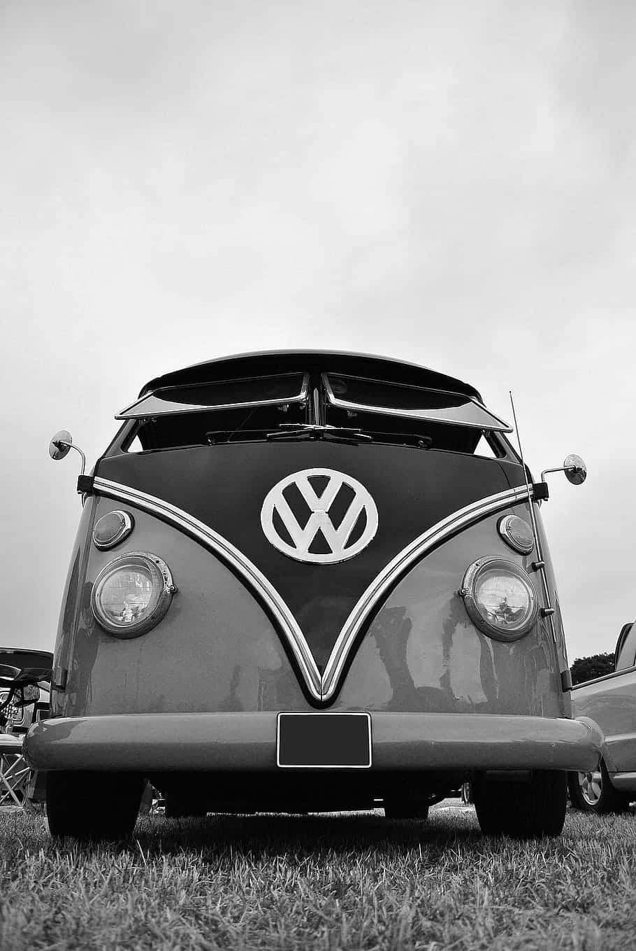 Black And White Vintage Car 桌布 壁紙 — 一輛經典黑白配色的福斯汽車巴士，帶有鍍鉻裝飾，在陰天下的草地上顯眼地停放。
